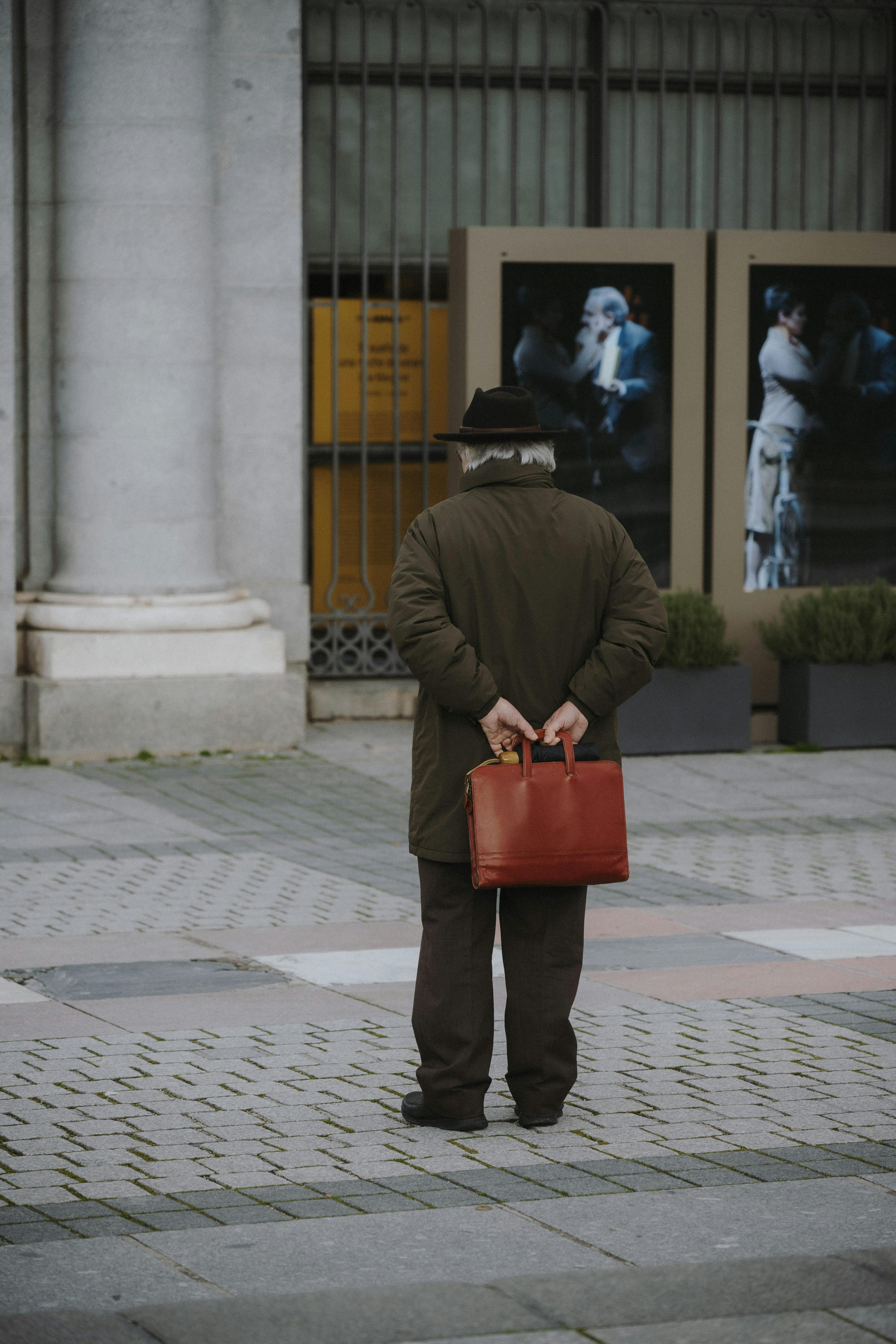 Free Senior man holding red briefcase in Madrid street. Urban life and culture. Stock Photo