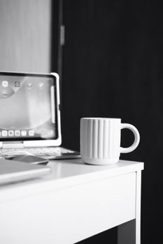 A minimalist black and white workspace with a tablet, keyboard, and coffee mug on a white desk.