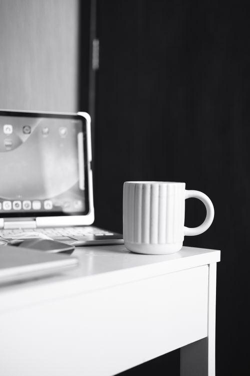 Free A minimalist black and white workspace with a tablet, keyboard, and coffee mug on a white desk. Stock Photo