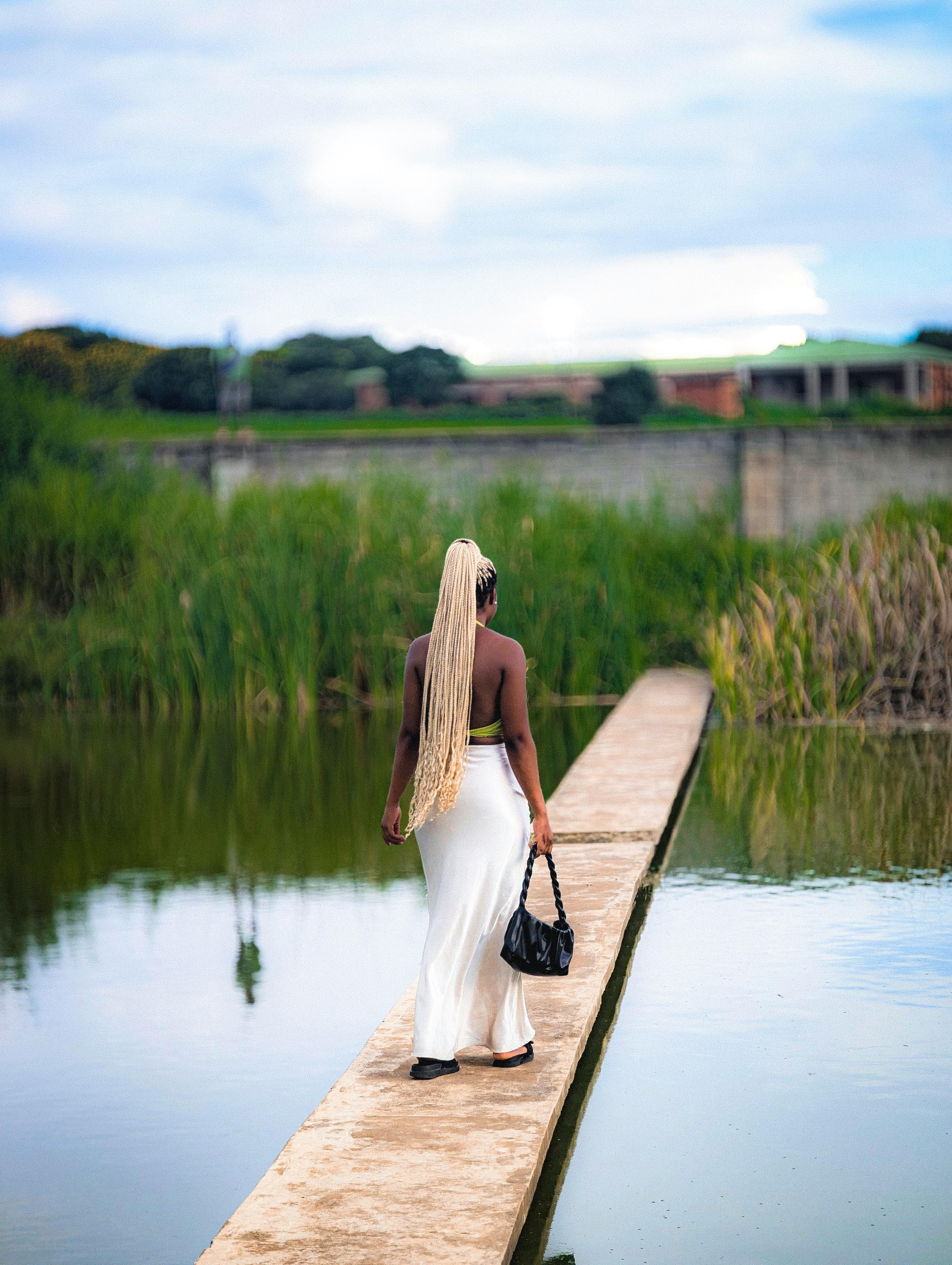 ingyenes Egy fehér ruhás nő sétál egy keskeny ösvényen, amelyet víz és nád vesz körül. Stockfotó