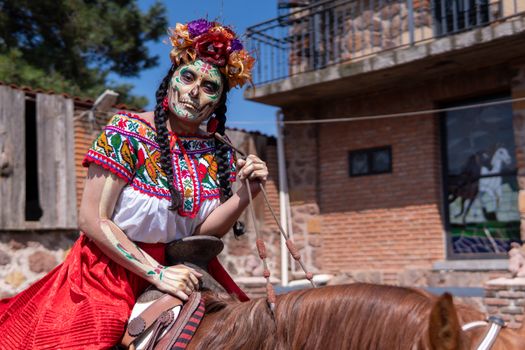 A woman in Catrina makeup and traditional Mexican attire rides a horse, celebrating cultural heritage.