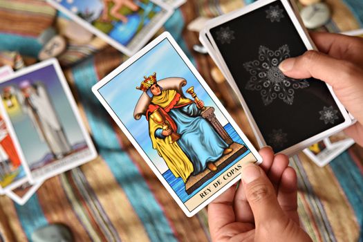Closeup of hands holding tarot card "Rey de Copas" on colorful fabric.