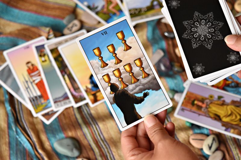 Close-up of a person holding tarot cards with a focus on the Seven of Cups card.