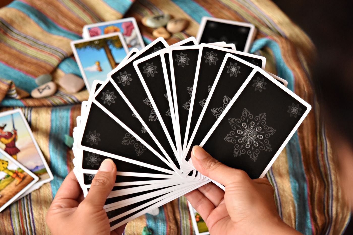 A pair of hands holding a fanned deck of cards face down over a woven cloth