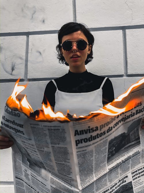 Free Woman in Black and White Tank Top Wearing Sunglasses While Holding Burning Newspaper Stock Photo