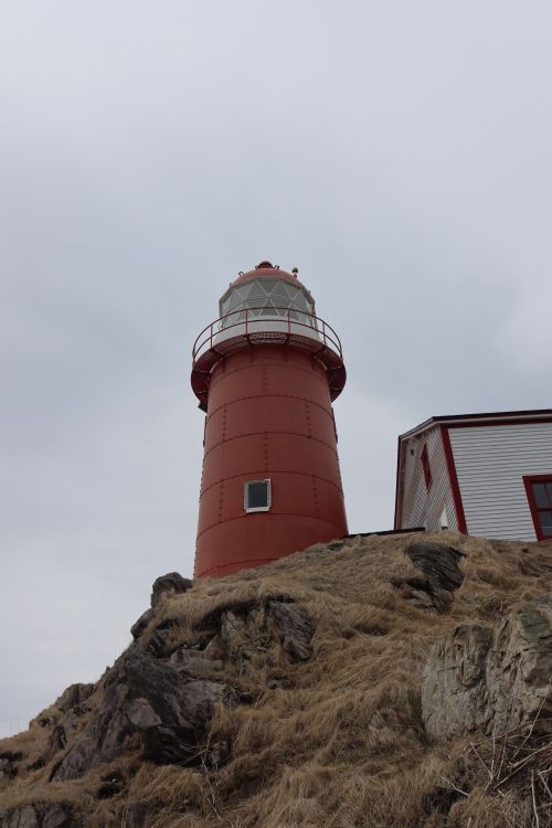 Free A striking red lighthouse stands tall on a rocky cliff under a cloudy sky. Stock Photo