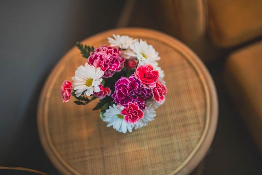 A lively bouquet of daisies and carnations arranged on a round wooden table, creating a charming indoor display.