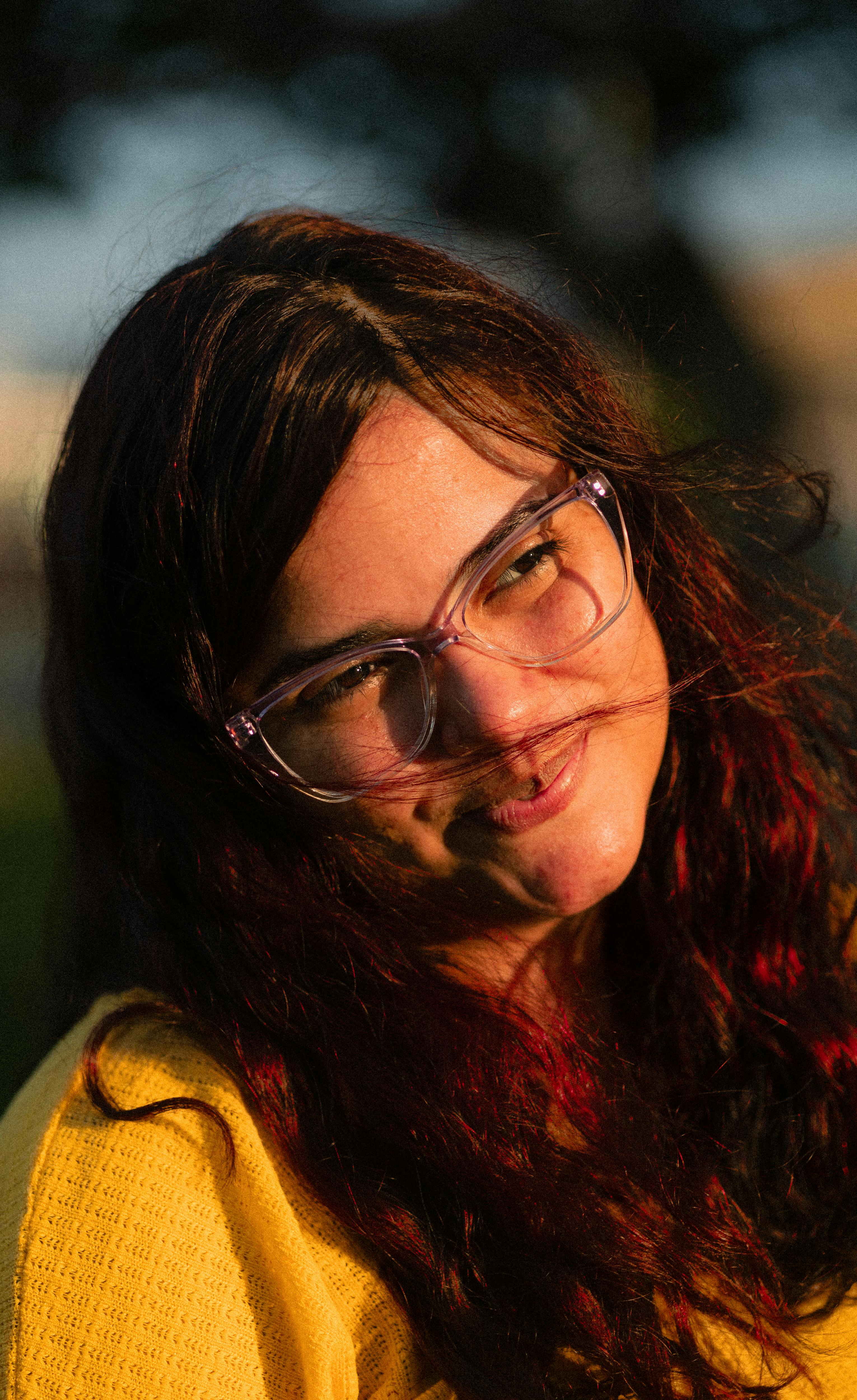 Gratis Ritratto di una donna sorridente con gli occhiali, illuminata dalla luce naturale durante l'ora d'oro. Foto a disposizione