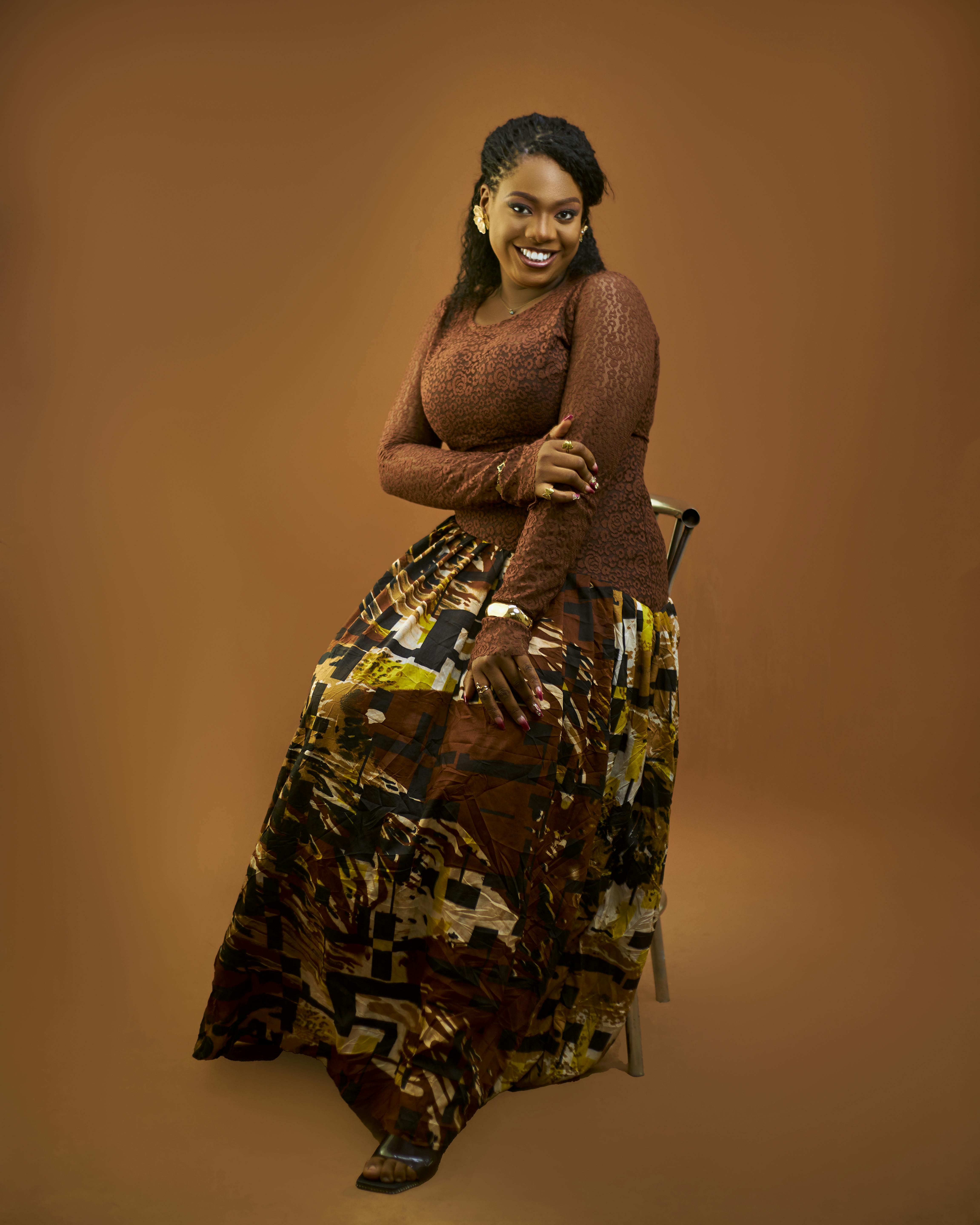 ingyenes Stílusos felnőtt nő elegáns öltözékben, barna háttér előtt ül, magabiztosságot és bájt sugározva. Stockfotó