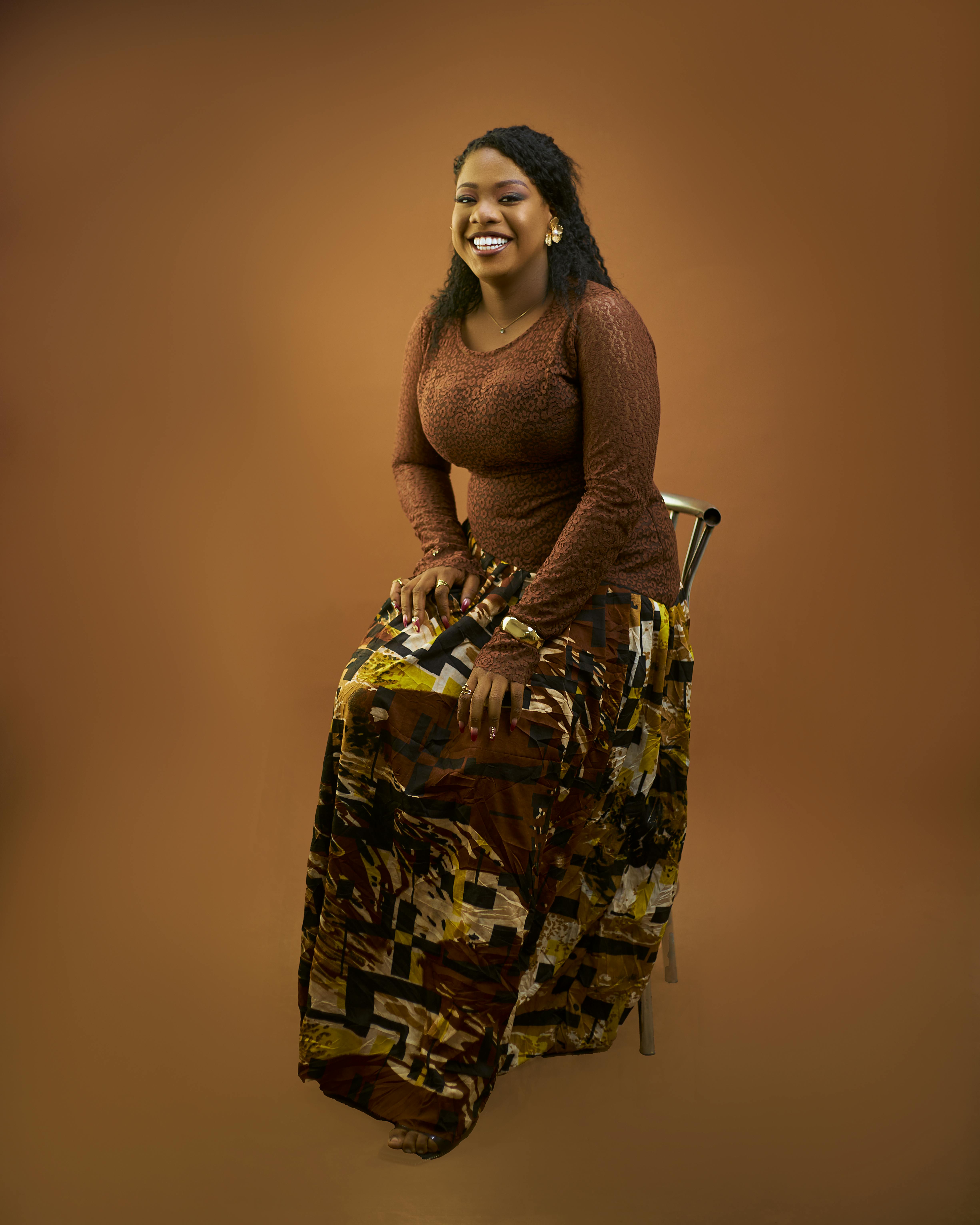 Gratis Ritratto di una donna sorridente che indossa abiti tradizionali africani su uno sfondo marrone caldo. Foto a disposizione