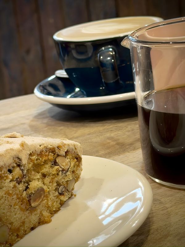 Cappuccino en tasse bleue, carafe de café filtre et part de gâteau aux amandes