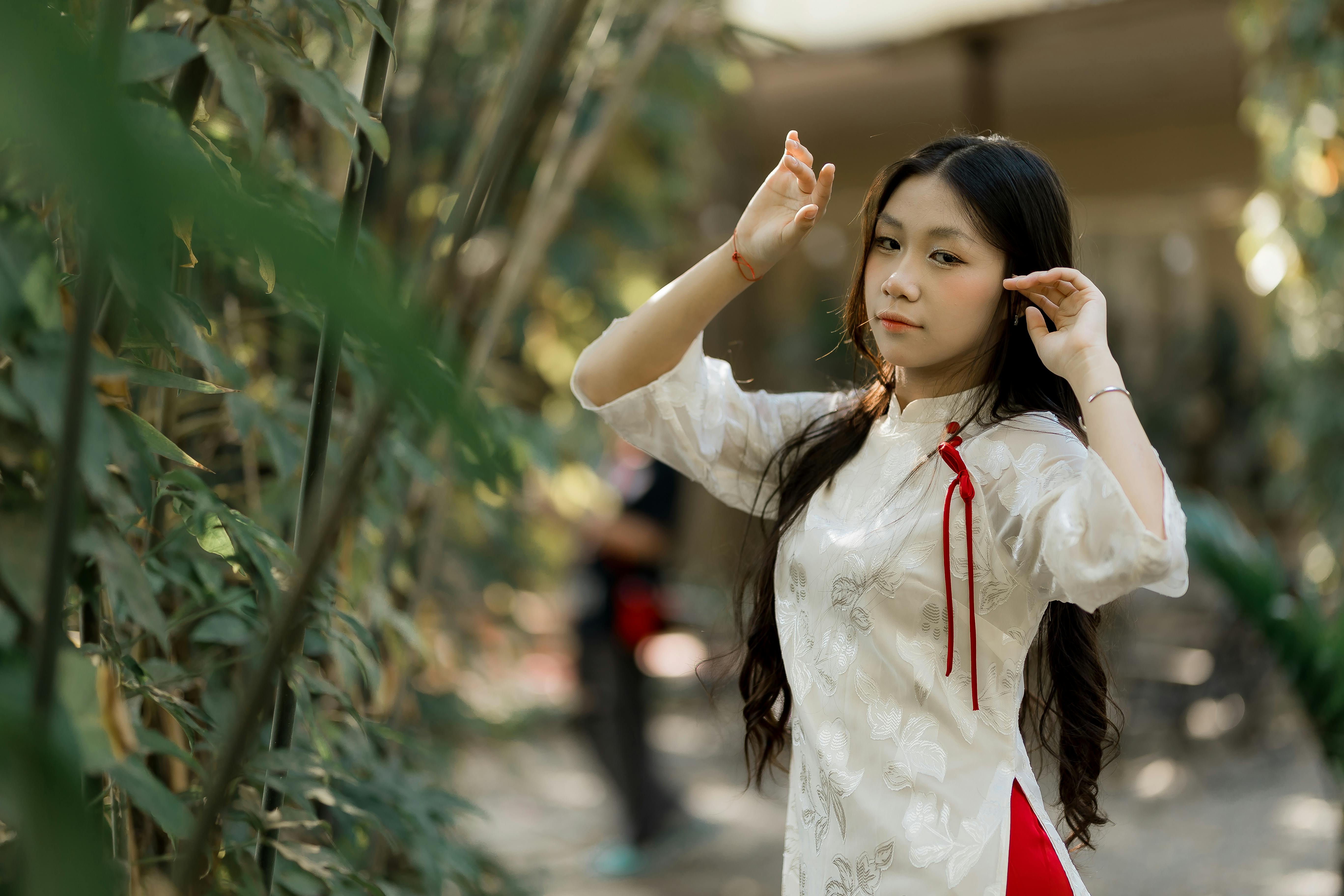 Gratis Una giovane donna con uno splendido abito tradizionale asiatico posa con grazia tra rigogliose piante verdi. Foto a disposizione