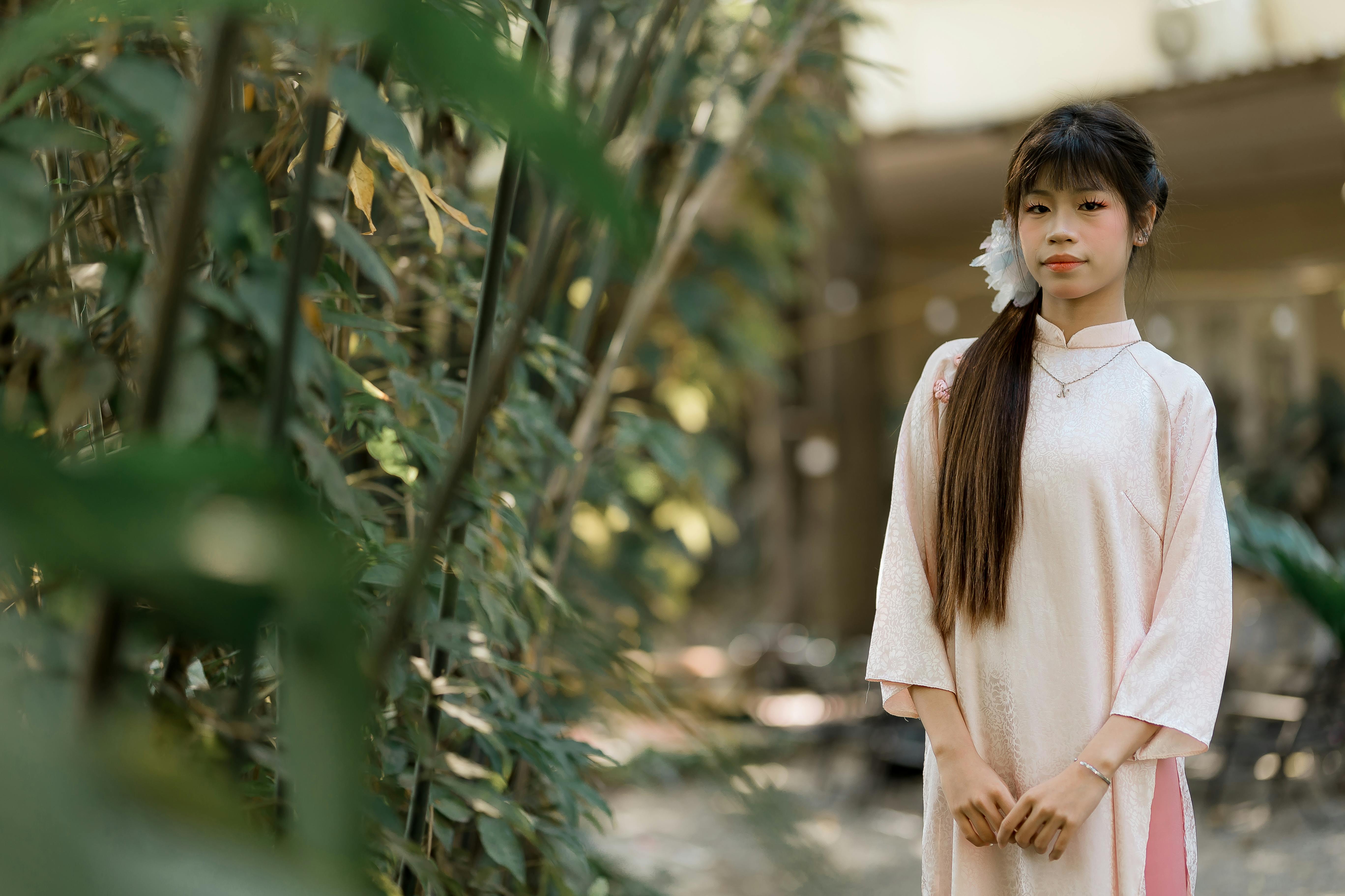 ฟรี หญิงสาวในชุดพื้นเมืองยืนอย่างสง่างามท่ามกลางป่าไผ่เขียวชอุ่ม โอบรับความสงบสุขของธรรมชาติ คลังภาพถ่าย