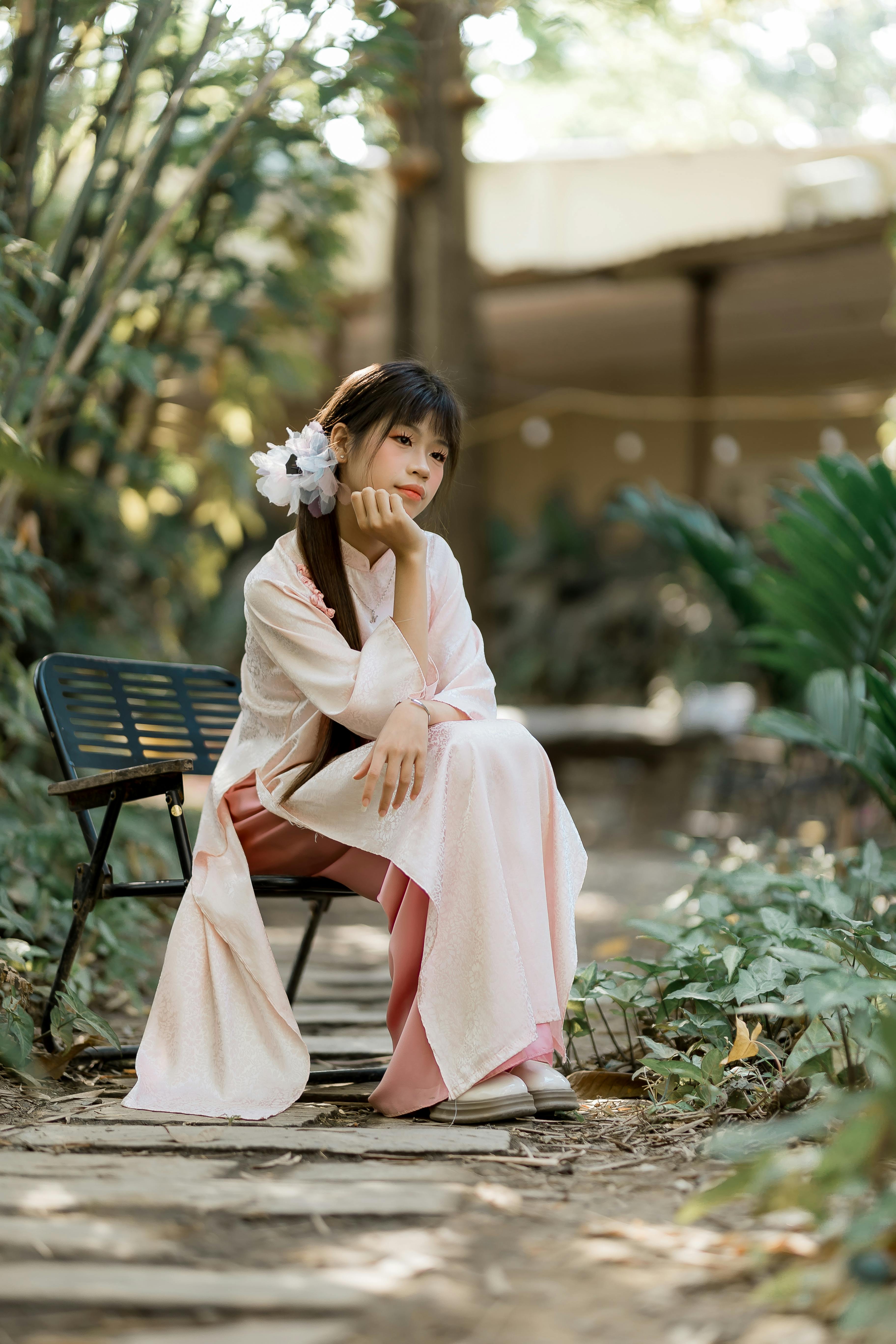 ฟรี หญิงสาวในชุดกิโมโนสีชมพูนั่งอย่างสง่างามในสวนอันเงียบสงบ ชวนให้รู้สึกถึงความสงบและการใคร่ครวญ คลังภาพถ่าย