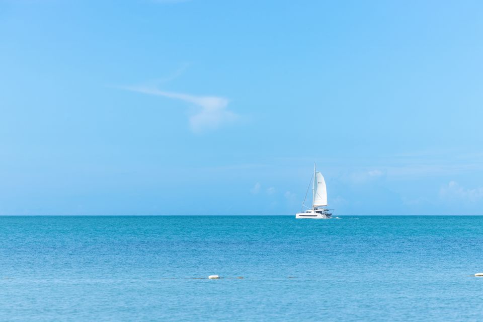 Small sailboat with white sail crossing calm open sea under a clear sky