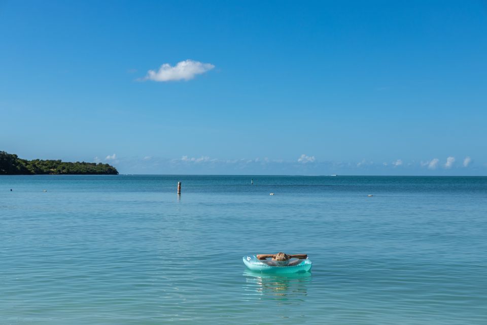 Person floating in a green inflatable raft on calm turquoise sea