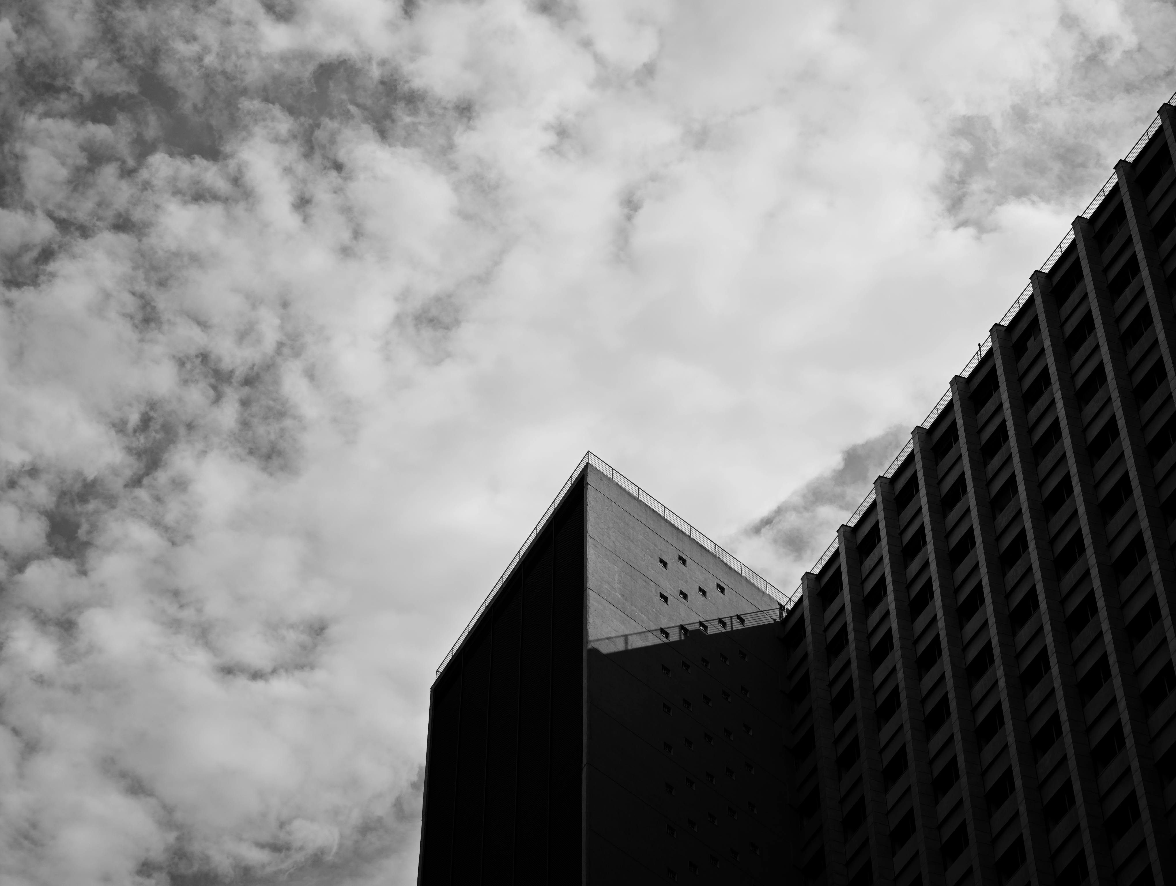 Ilmainen Mustavalkoinen valokuva korkeasta modernista rakennuksesta pilvistä taivasta vasten. Kuvapankkikuva