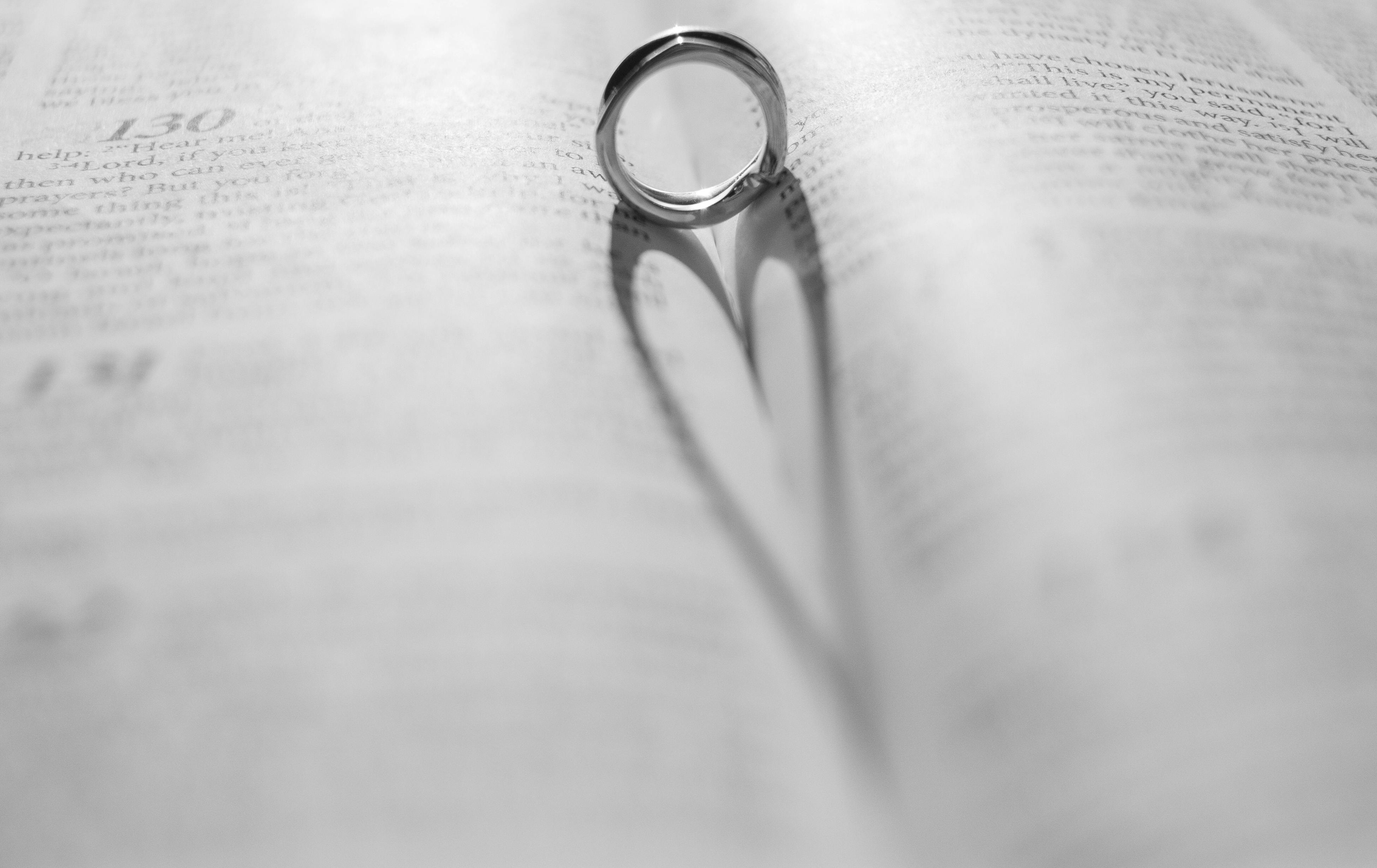 Bezpłatne Obrączka ślubna rzuca cień w kształcie serca na otwartą stronę czarno-białej książki. Zdjęcie z galerii