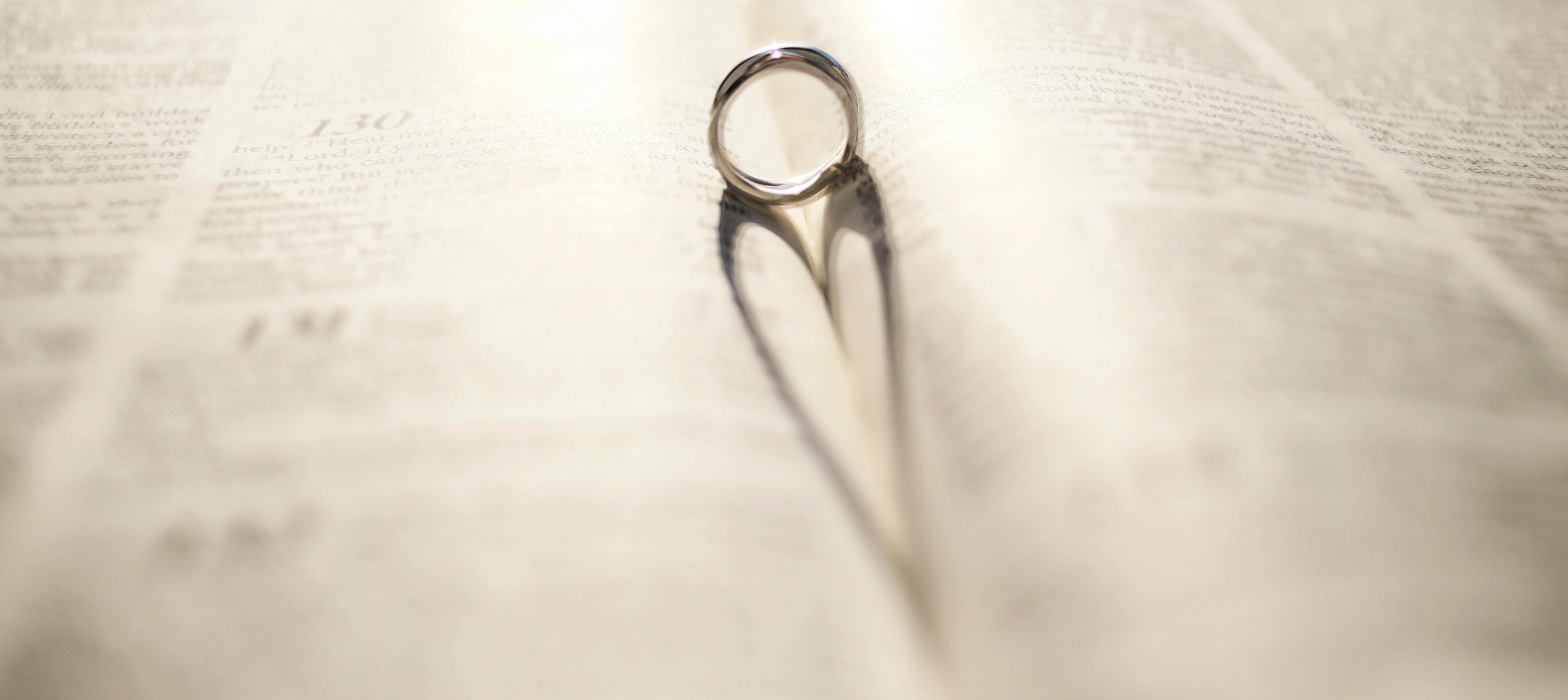 Gratuit O verighetă de argint aruncând o umbră în formă de inimă pe o pagină deschisă de carte. Fotografie de stoc