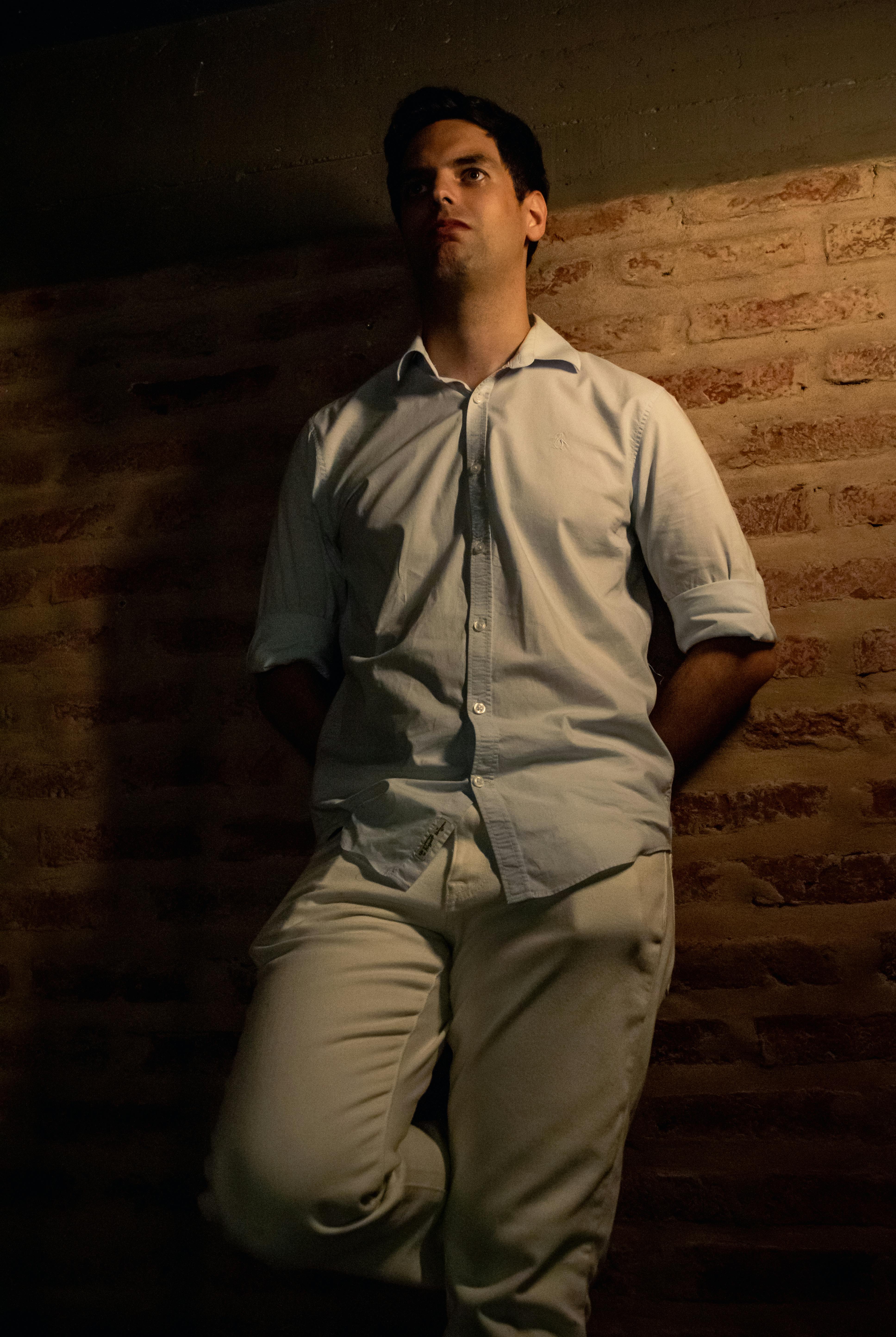 Portrait of a man standing against a brick wall, dim lighting for a dramatic effect.