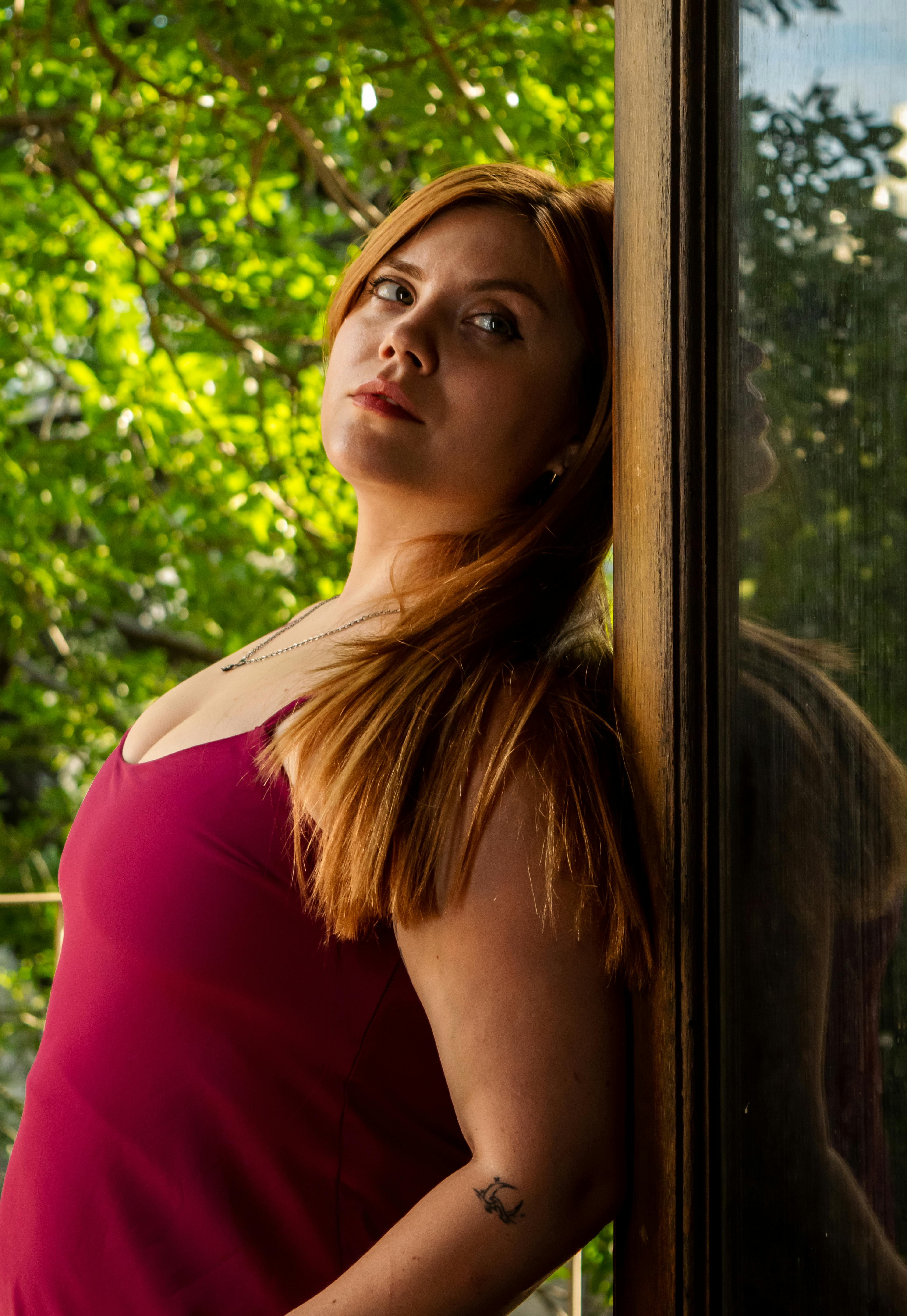 Gratis Giovane donna in abito rosso appoggiata a uno specchio, circondata dalla natura. Foto a disposizione