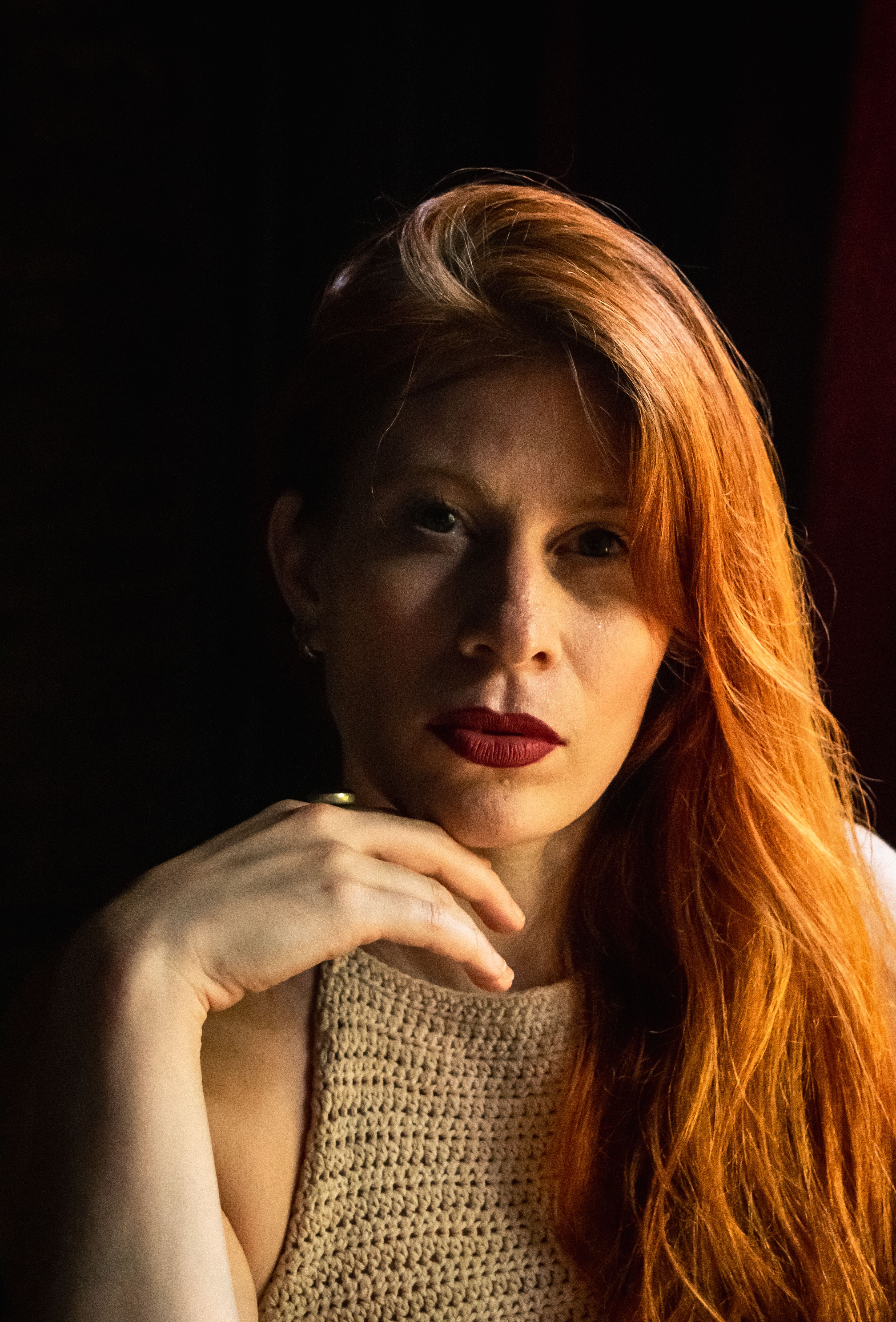 A captivating portrait capturing a woman with red hair in warm lighting, evoking a sense of mystery and introspection.