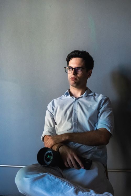 Free Pensive man in white shirt sits with a camera, casting a thoughtful gaze. Stock Photo