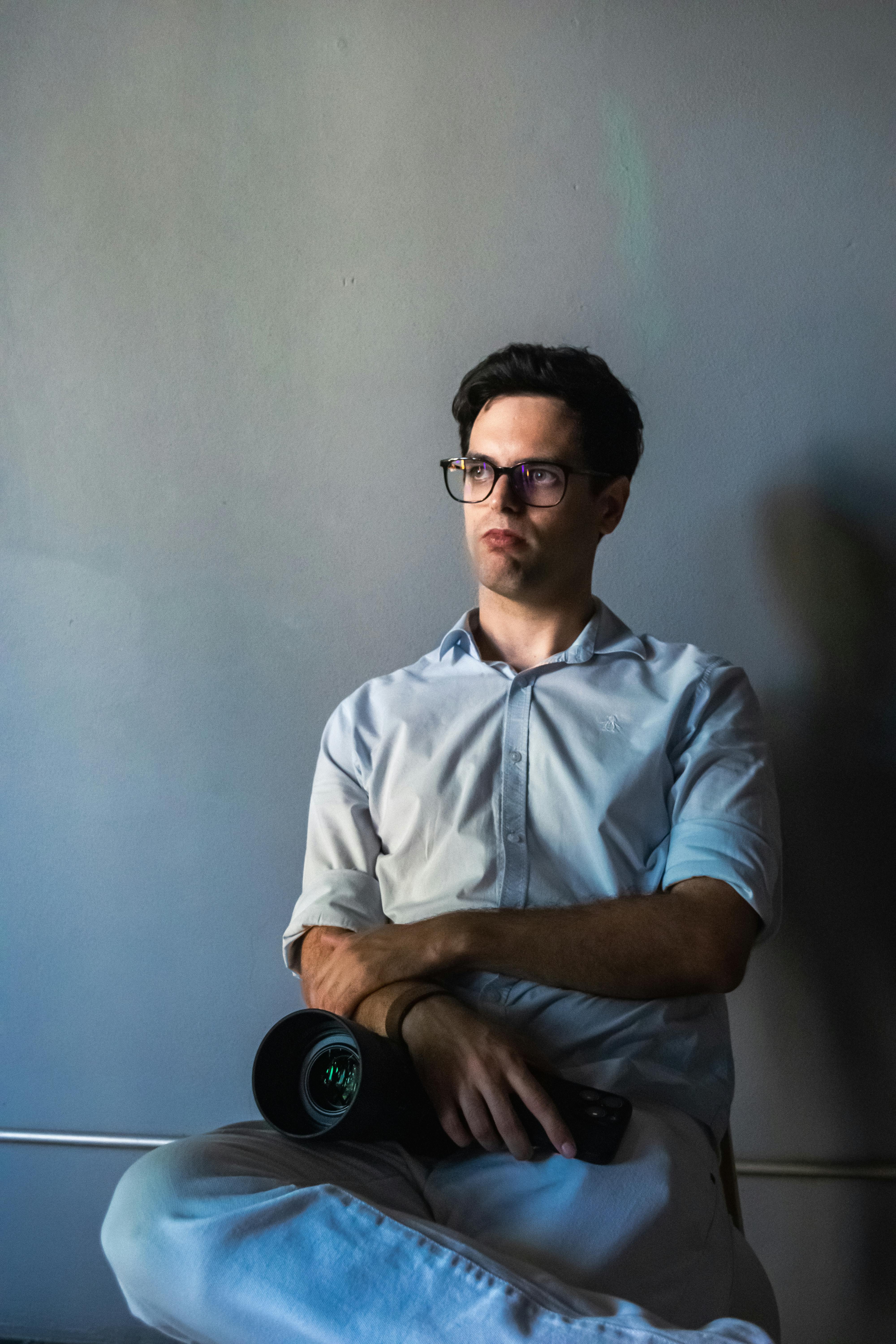 Gratis Un uomo pensieroso, in camicia bianca, è seduto con una macchina fotografica e lancia un'occhiata pensierosa. Foto a disposizione