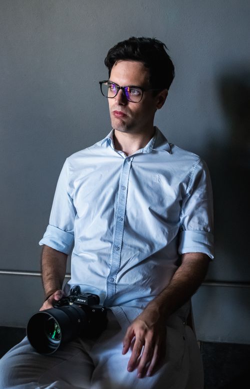 Free A young male photographer in a studio holding a camera, looking thoughtful. Stock Photo