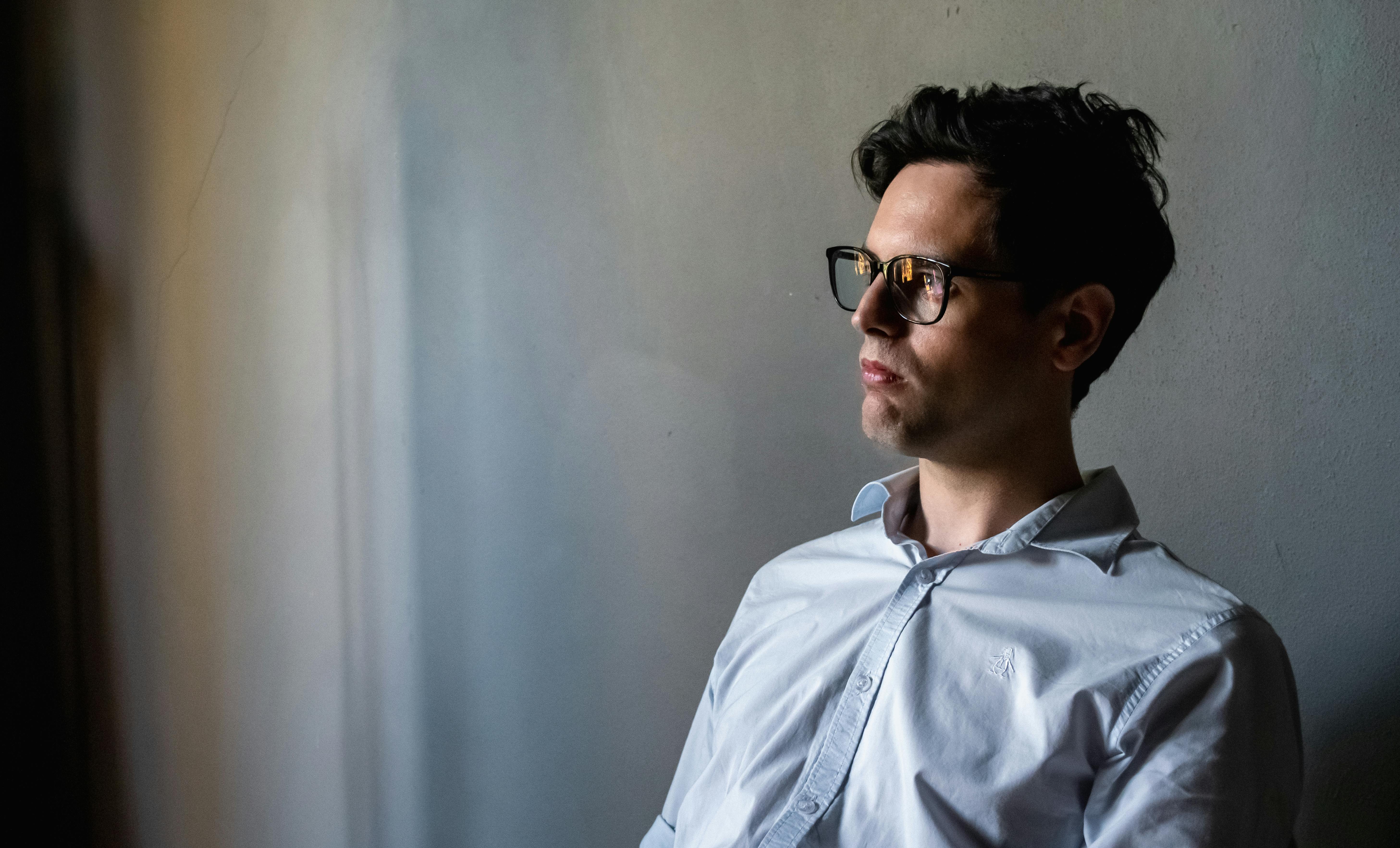 Gratis Un uomo con gli occhiali guarda contemplativamente nel vuoto in un interno. Foto a disposizione