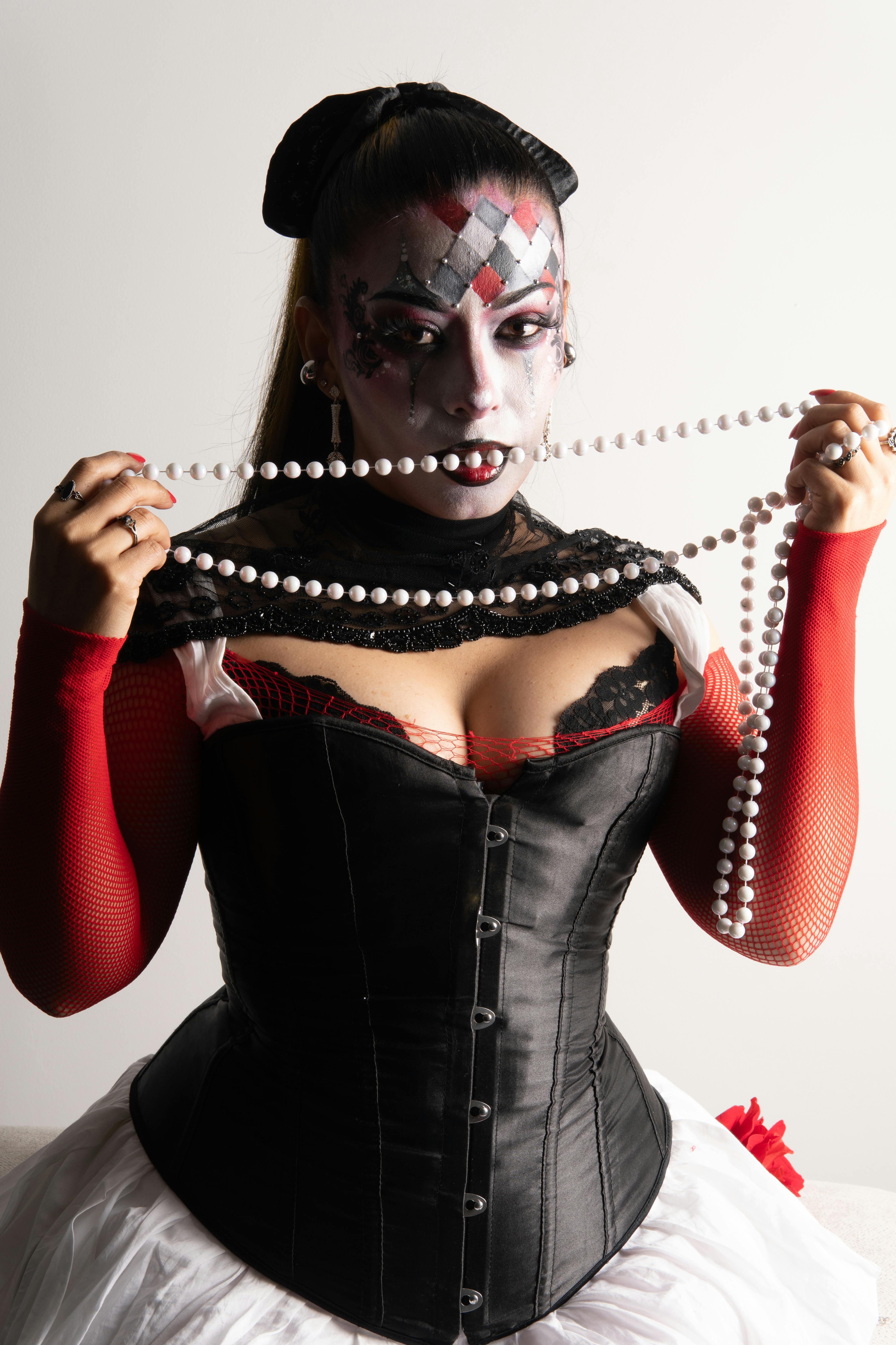 Ücretsiz Beyaz bir arka plan önünde, dramatik makyajlı ve palyaço kostümü giymiş bir kadın inci boncuklar tutuyor. Stok Fotoğraflar