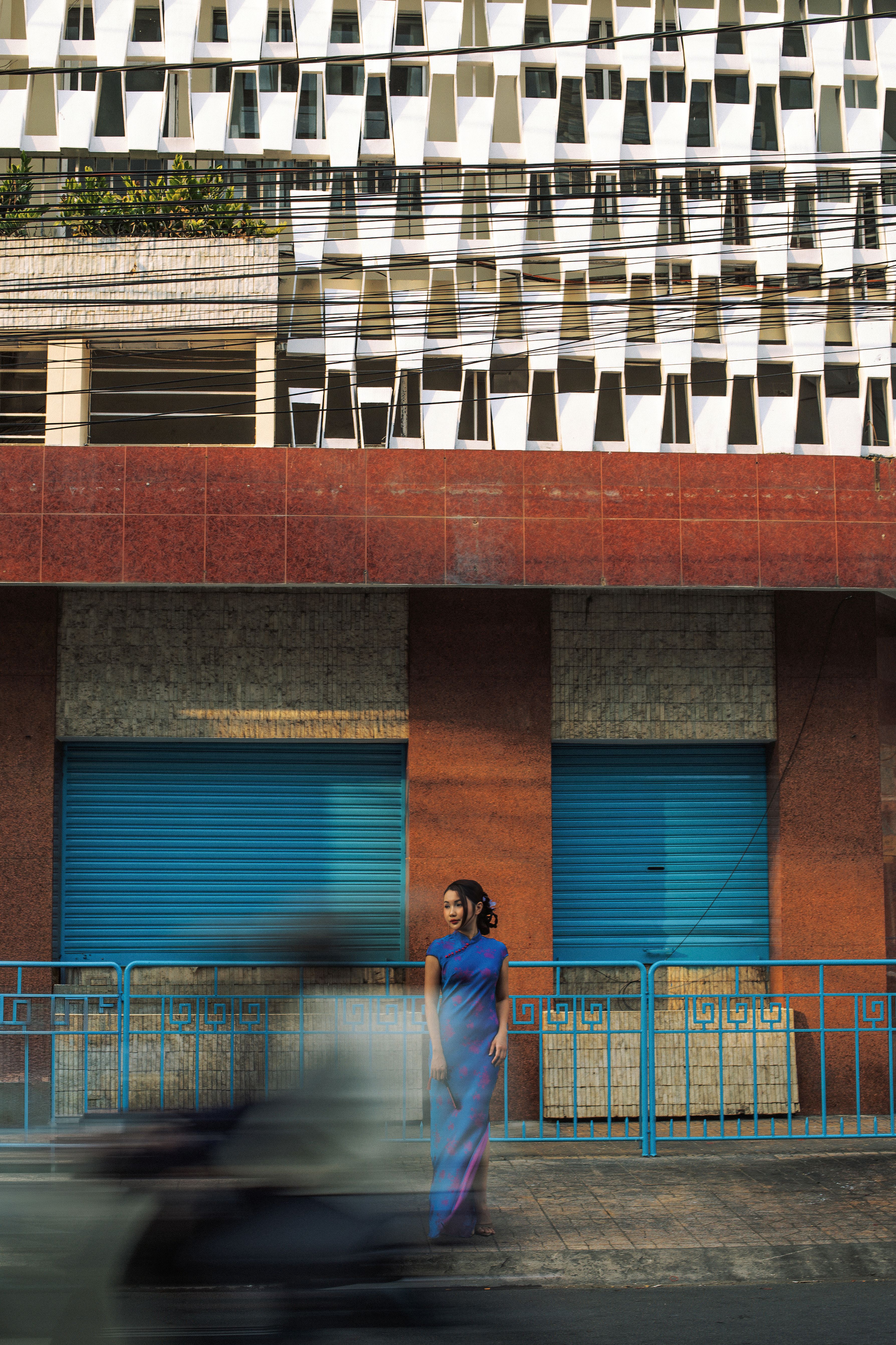 Blurred motion of a street with a woman in a blue dress in front of an urban building facade.