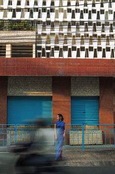 Blurred motion of a street with a woman in a blue dress in front of an urban building facade.