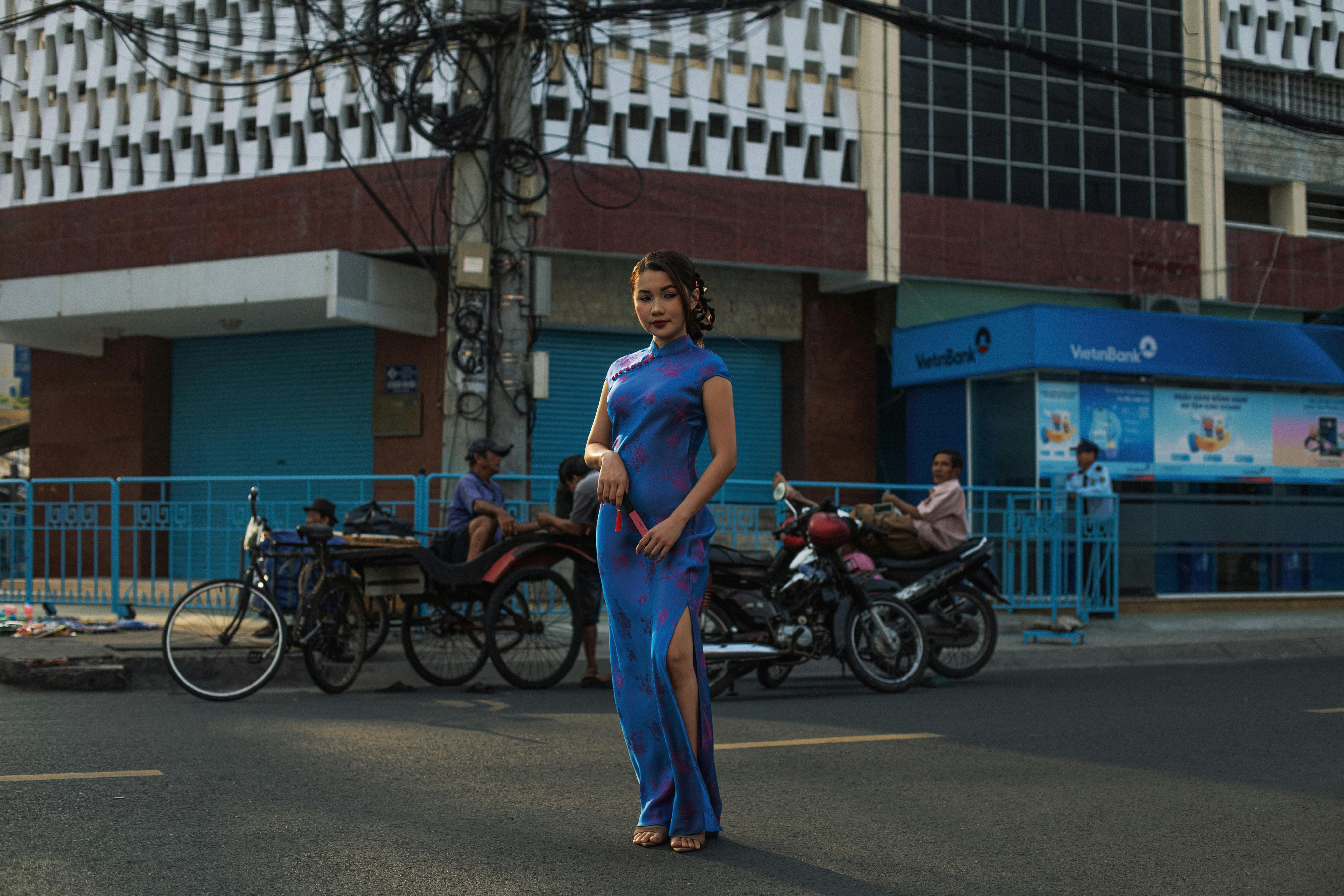 ฟรี หญิงสาวในชุดพื้นเมืองสีน้ำเงินยืนโพสท่าอย่างมั่นใจบนถนนในเมืองที่คึกคัก คลังภาพถ่าย