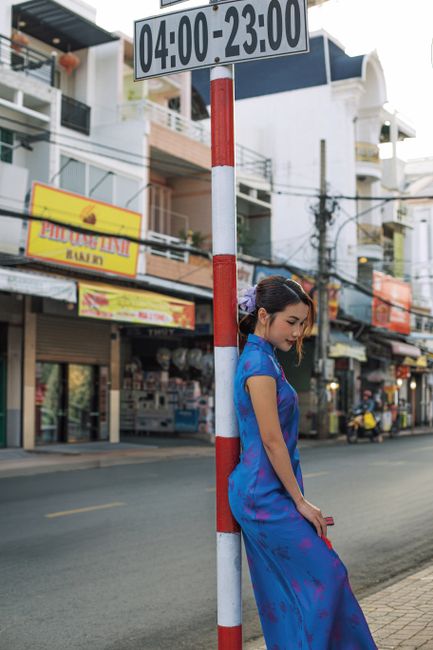 Woman in a vibrant blue cheongsam poses by a city street sign in an urban setting.