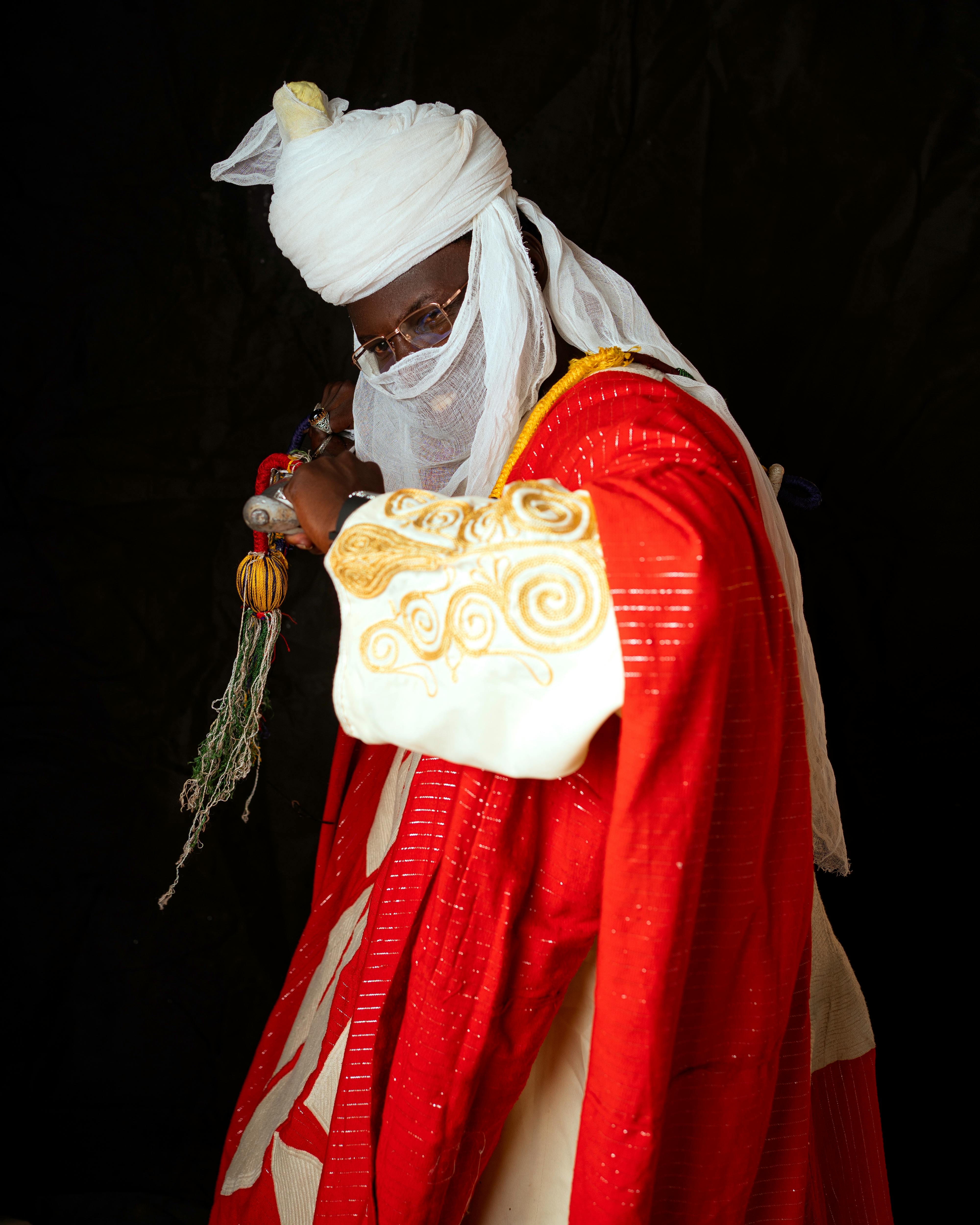 Portrait of a Nigerian tribal leader in traditional regalia holding ceremonial items.