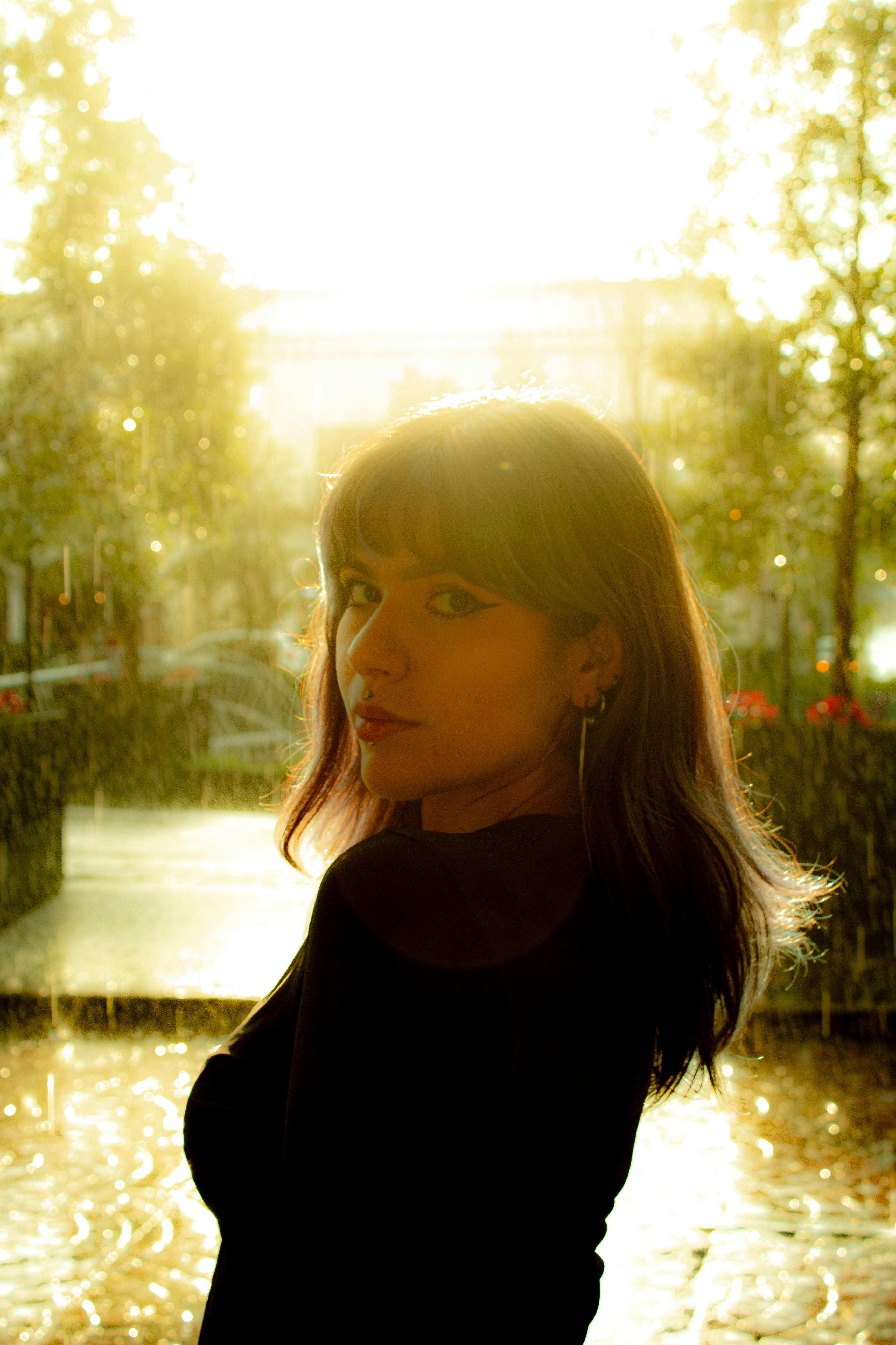 Free A woman poses elegantly in the golden light of a sunset rain, creating a serene and dreamy atmosphere. Stock Photo