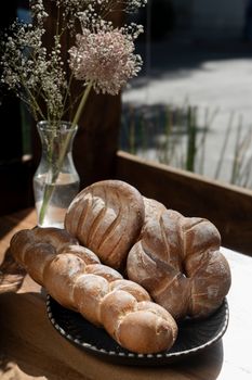 Delicious artisanal bread on a platter with vase of flowers on a sunny day.