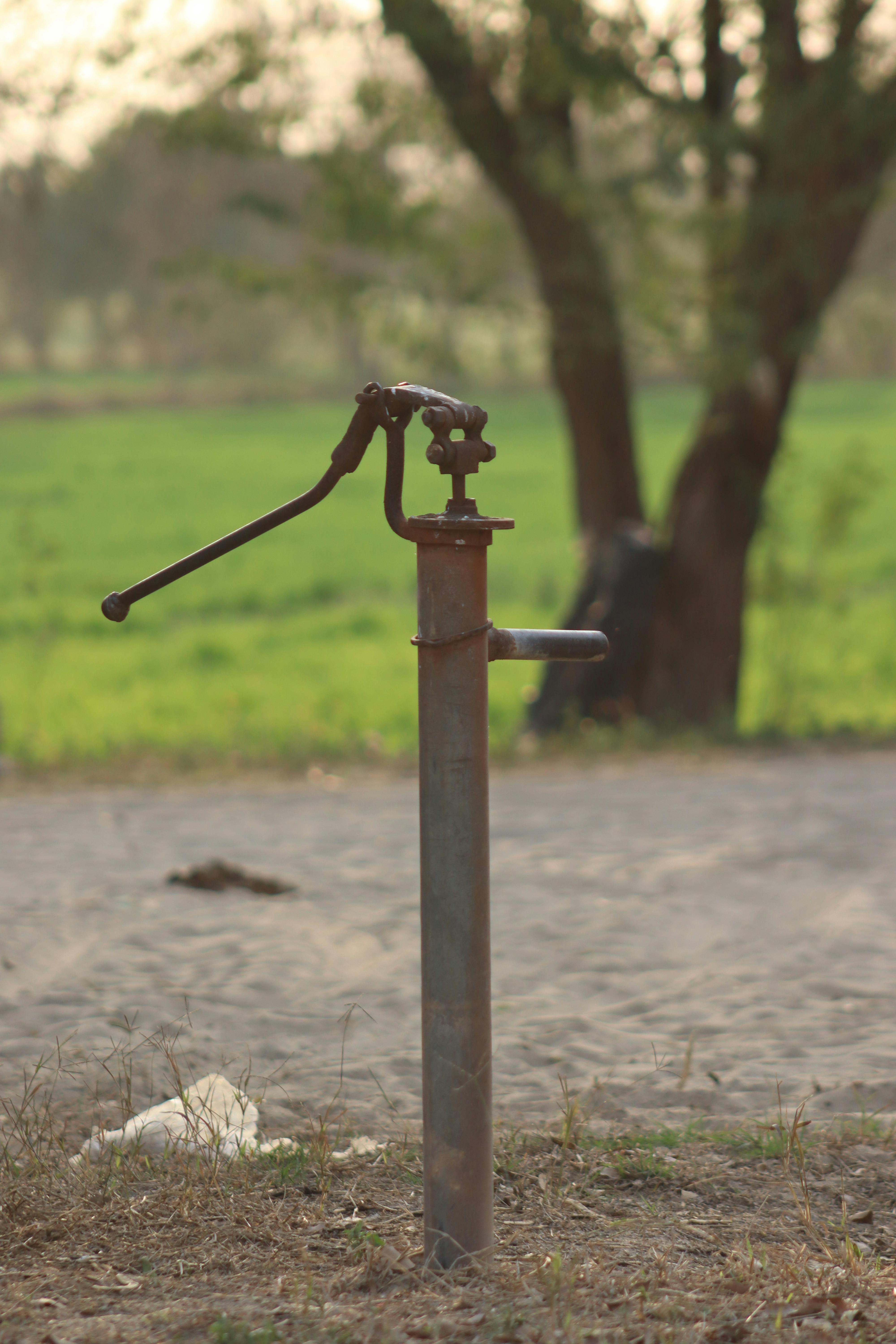 gratis Rustieke waterpomp met een natuurlijke achtergrond van groene velden en zacht zonlicht. Stockfoto