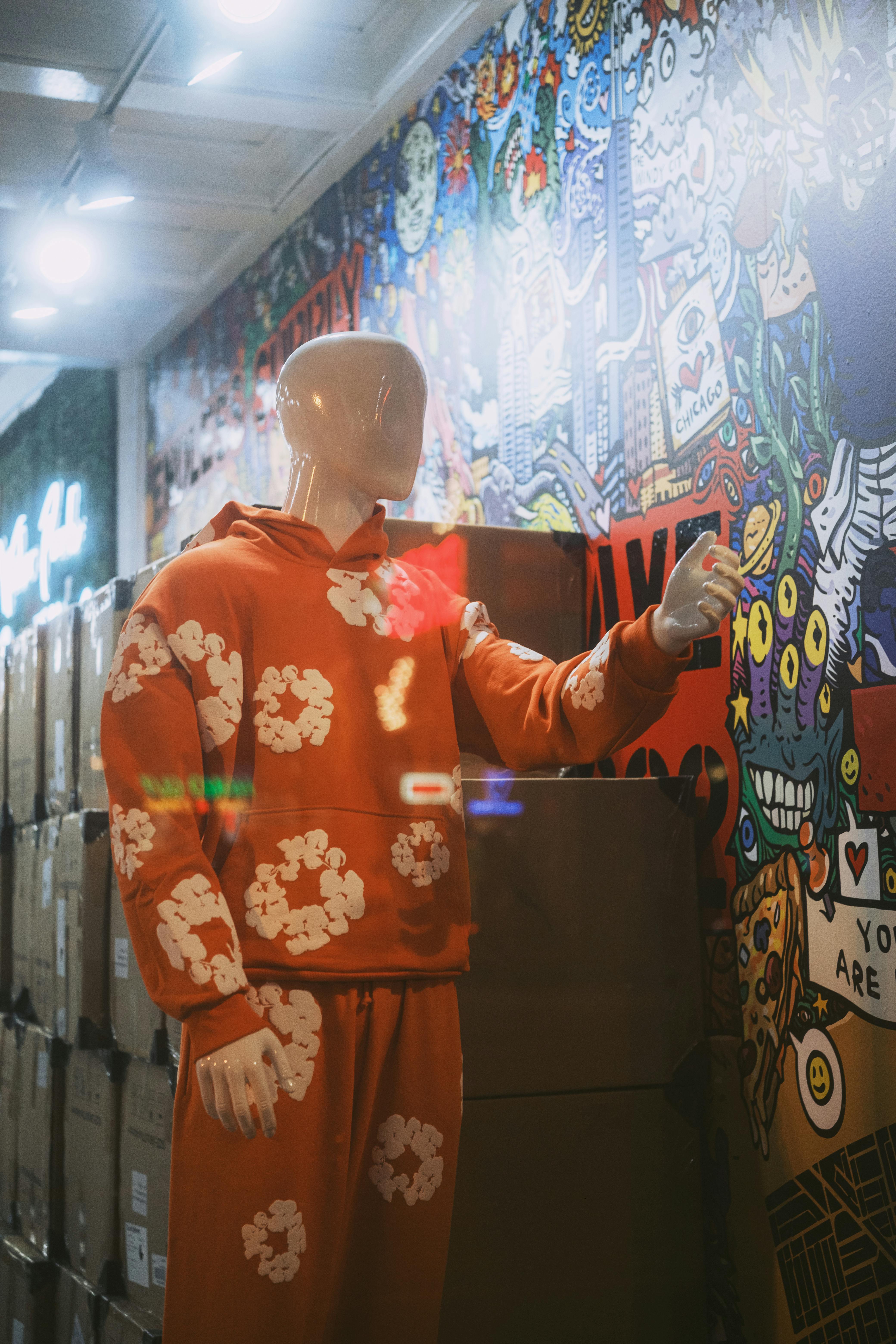 De franc Un maniquí elegant amb un xandall floral taronja posa al costat d'un vibrant mural d'art urbà, afegint-hi un toc de color i creativitat. Foto d'estoc