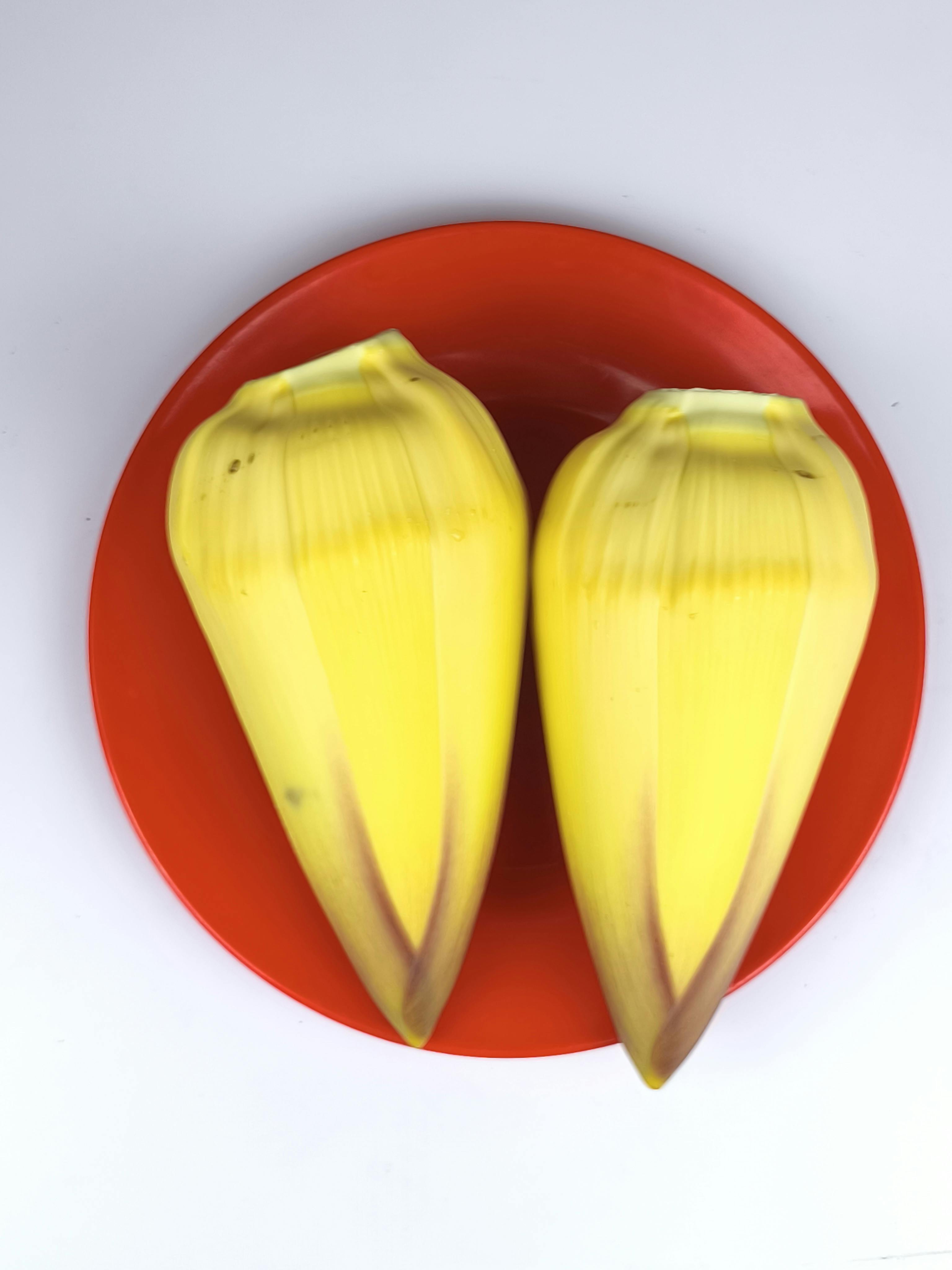 Miễn phí Hai bông hoa chuối màu vàng tươi được đặt trên một chiếc đĩa màu đỏ rực rỡ theo kiểu bố cục phẳng. Ảnh lưu trữ