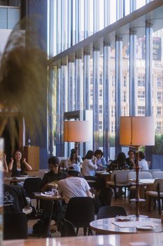 A bustling modern cafe with large windows and natural light, filled with people.