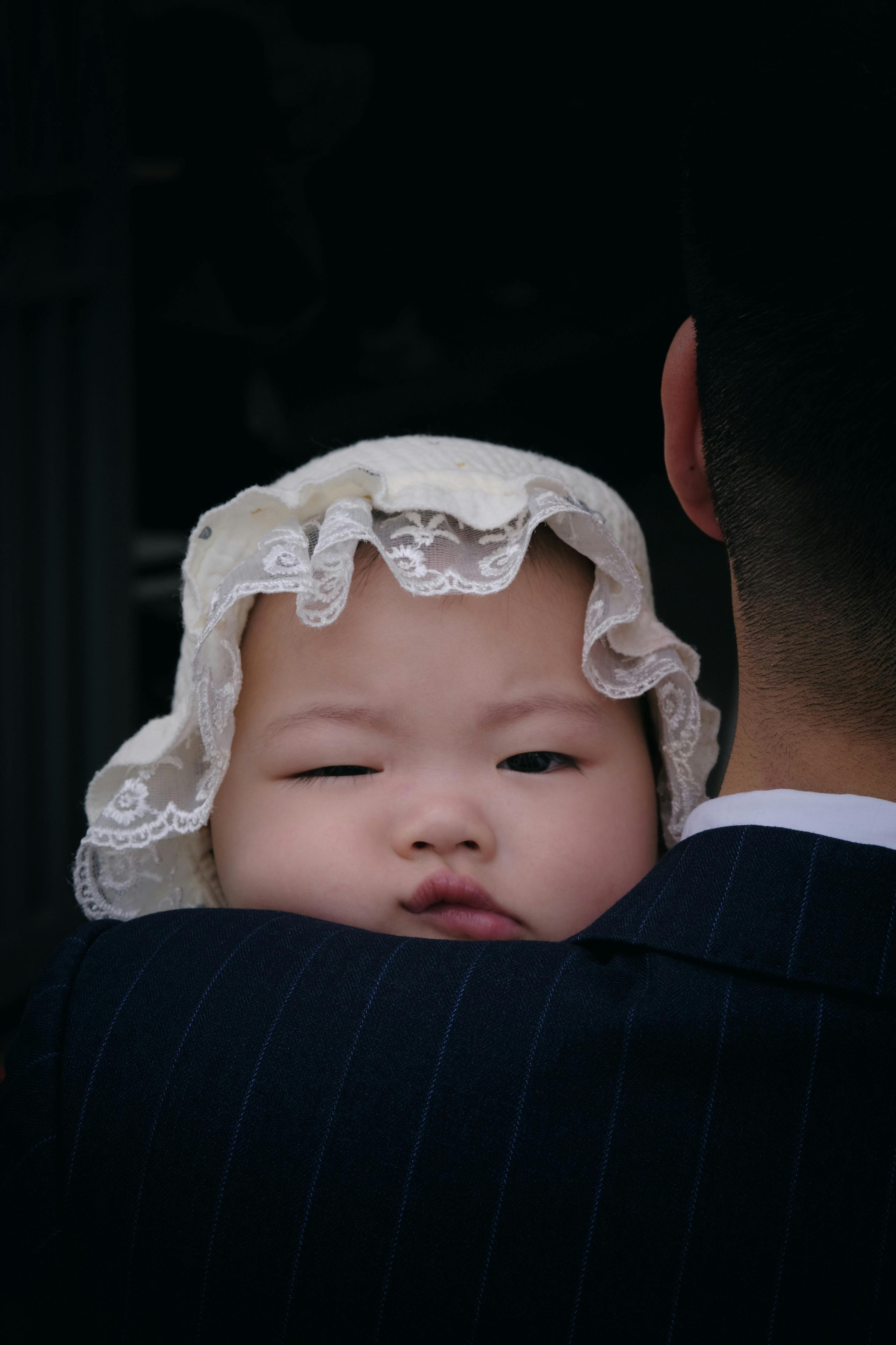 Δωρεάν Κοντινό πλάνο ενός μωρού με λευκό σκουφάκι που το κρατάει ένας ενήλικας σε εσωτερικό χώρο. Φωτογραφία από στοκ φωτογραφιών