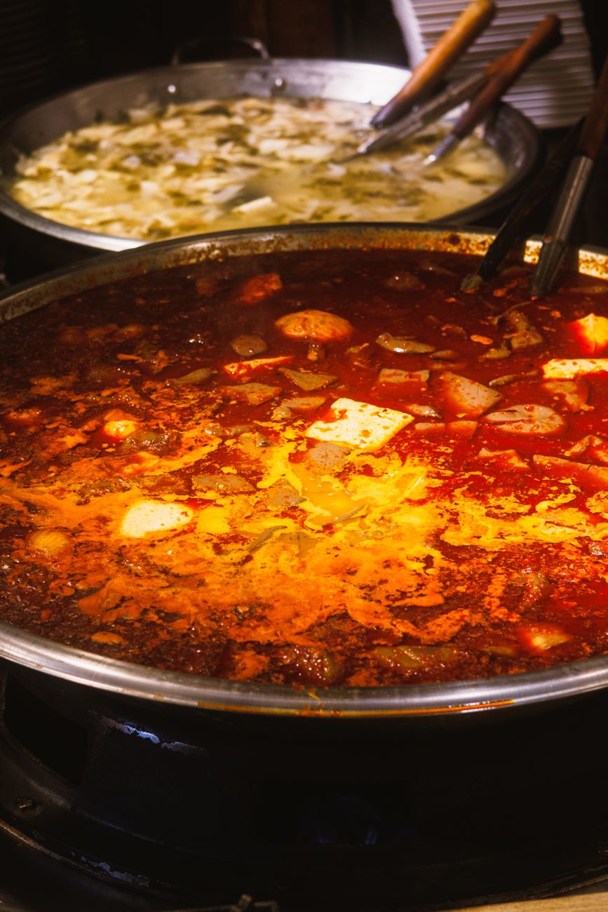 Bubbling Szechuan hot pot with bright red chili oil broth, raw ingredients, and chopsticks