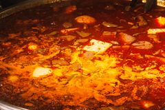 Close-up of a spicy red hot pot dish served in a large metal bowl indoors.