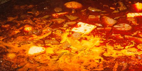 Close-up of a spicy red hot pot dish served in a large metal bowl indoors.