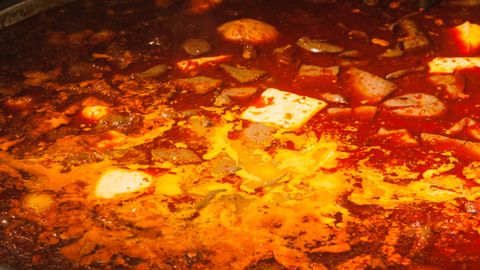 Close-up of a spicy red hot pot dish served in a large metal bowl indoors.