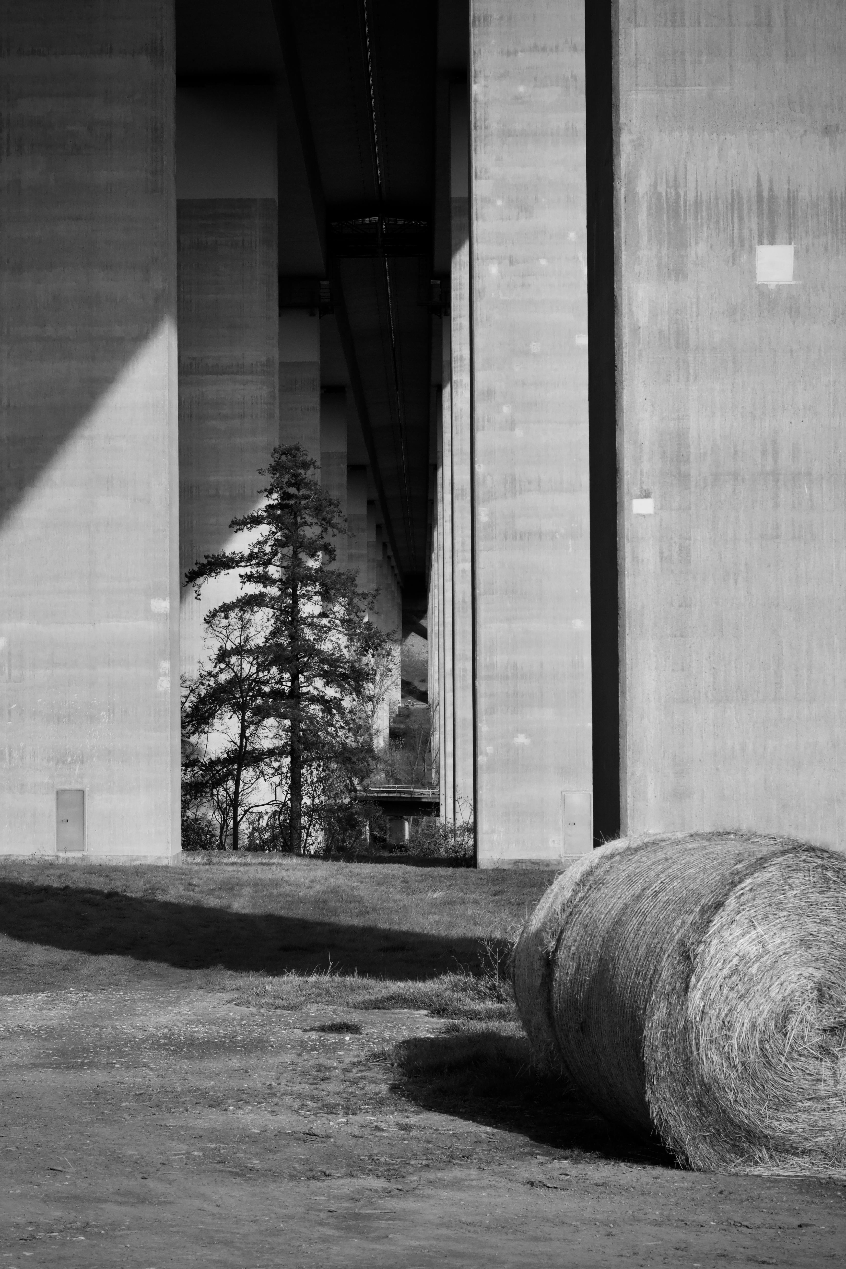 Ücretsiz Kırsal ve kentsel zıtlığı yakalayan, saman balyalarıyla çevrili bir şehir köprüsünün siyah beyaz fotoğrafı. Stok Fotoğraflar