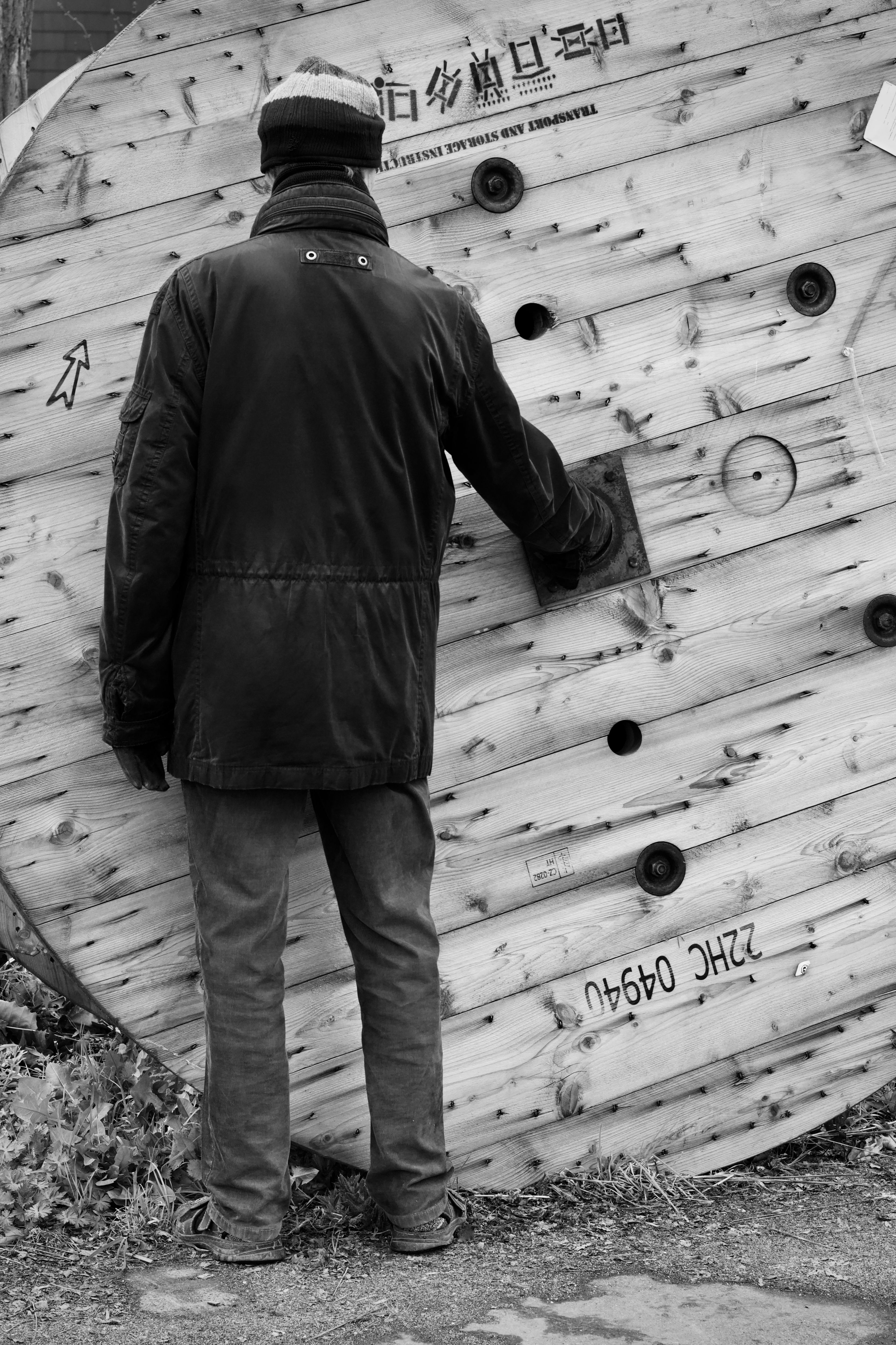 An adult male examines a large wooden cable spool in a black and white image.