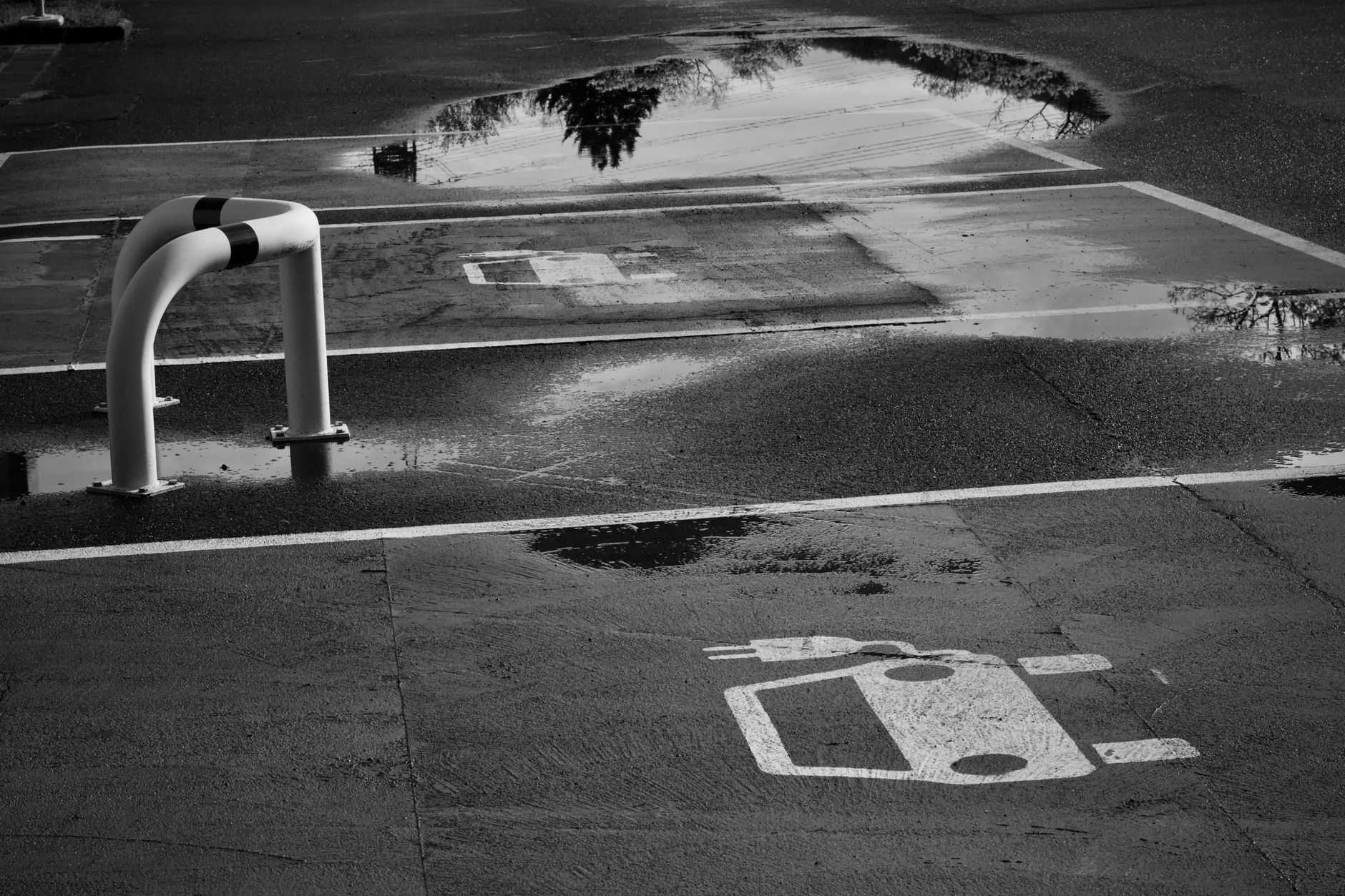 A black and white photo of an empty electric car parking spot with water reflections showcasing a serene and urban environment.